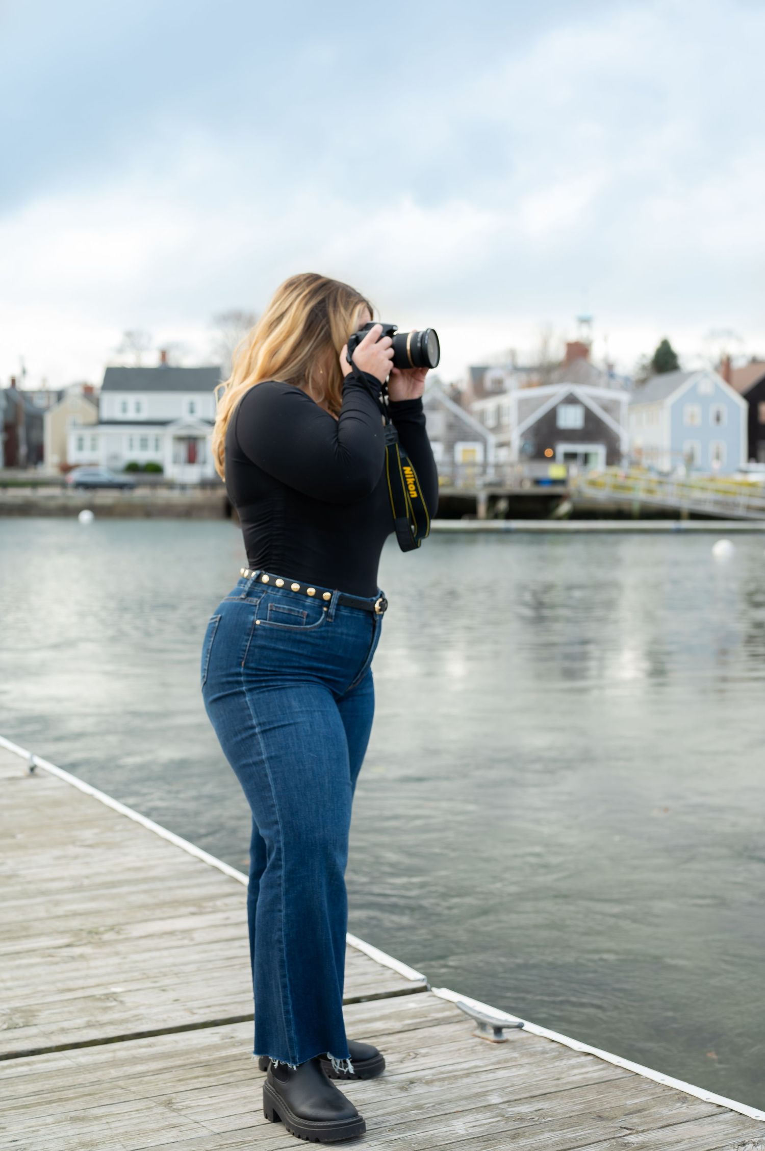 Photographer takes photos from a wooden dock overlooking colorful coastal homes in New England.