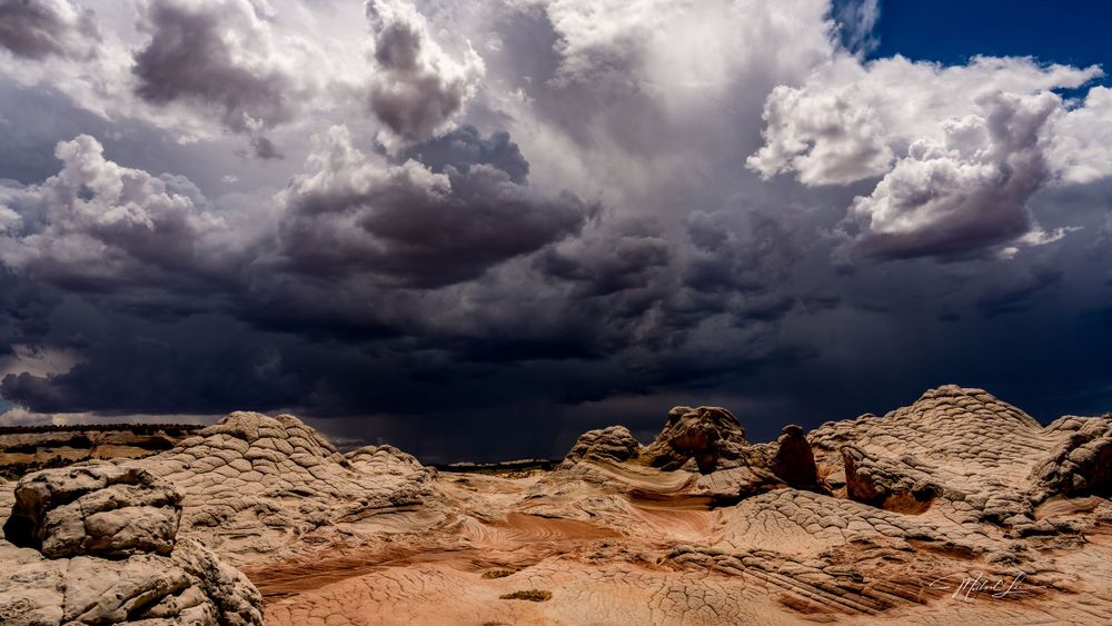 Dramatic storm clouds gather over red rock formations in the desert landscape.