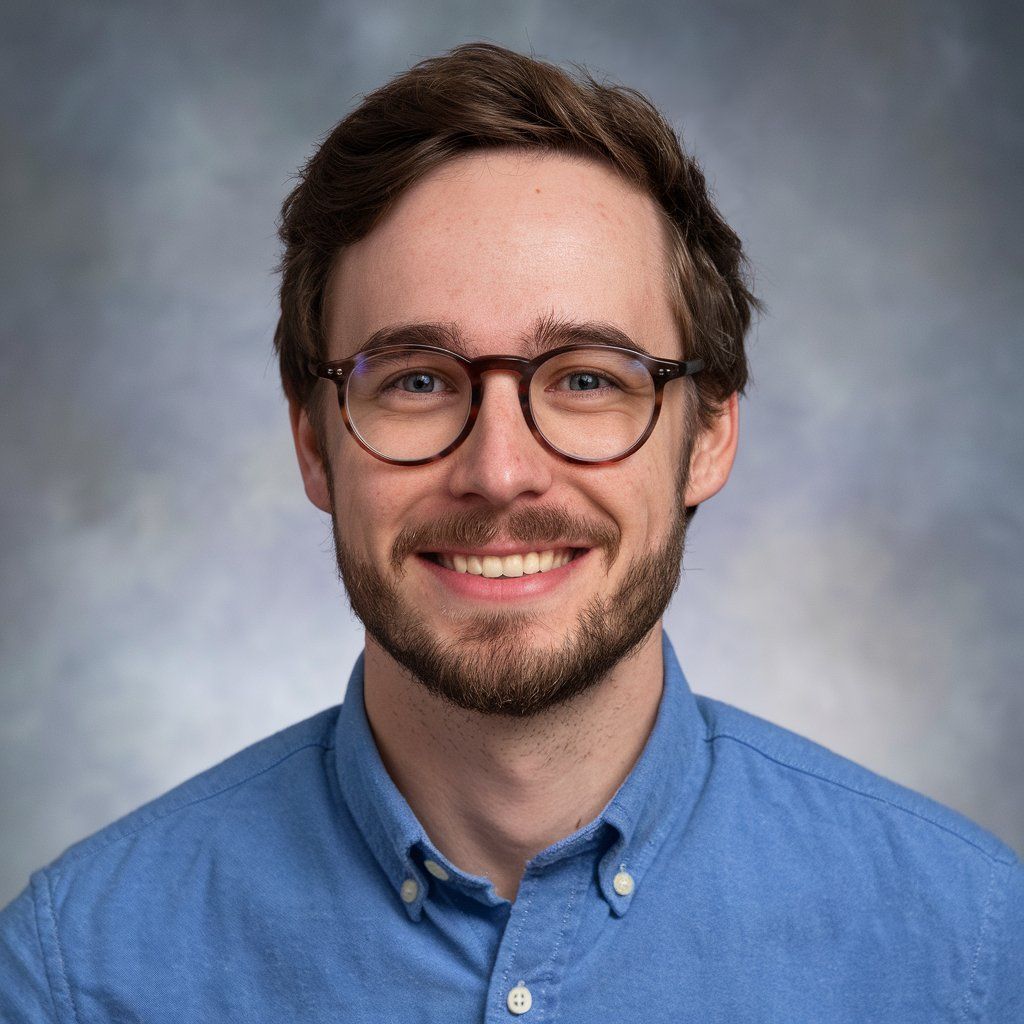 Professional headshot of a person in glasses and blue button-down shirt against a gray background.