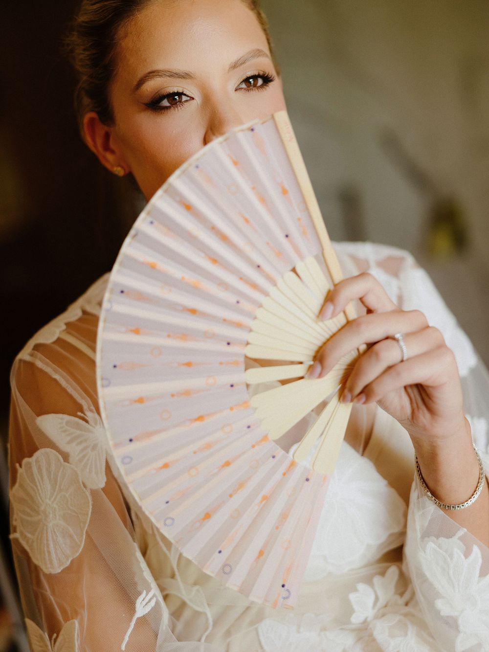 A decorative white folding fan with sparkly details held up against a white dress.