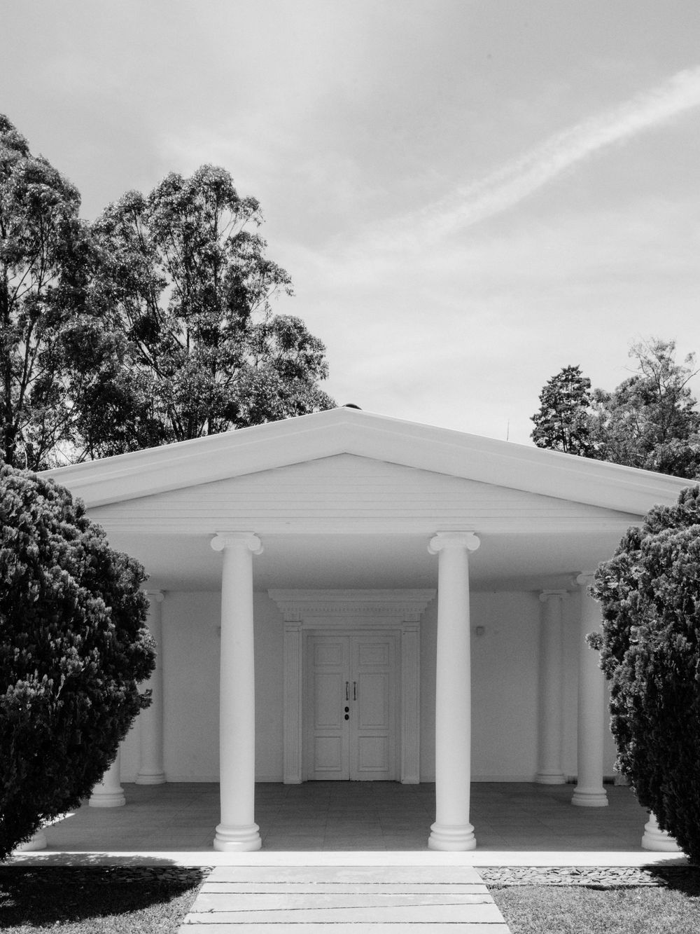 Classical white wedding chapel entrance with tall columns and eucalyptus trees in black and white.