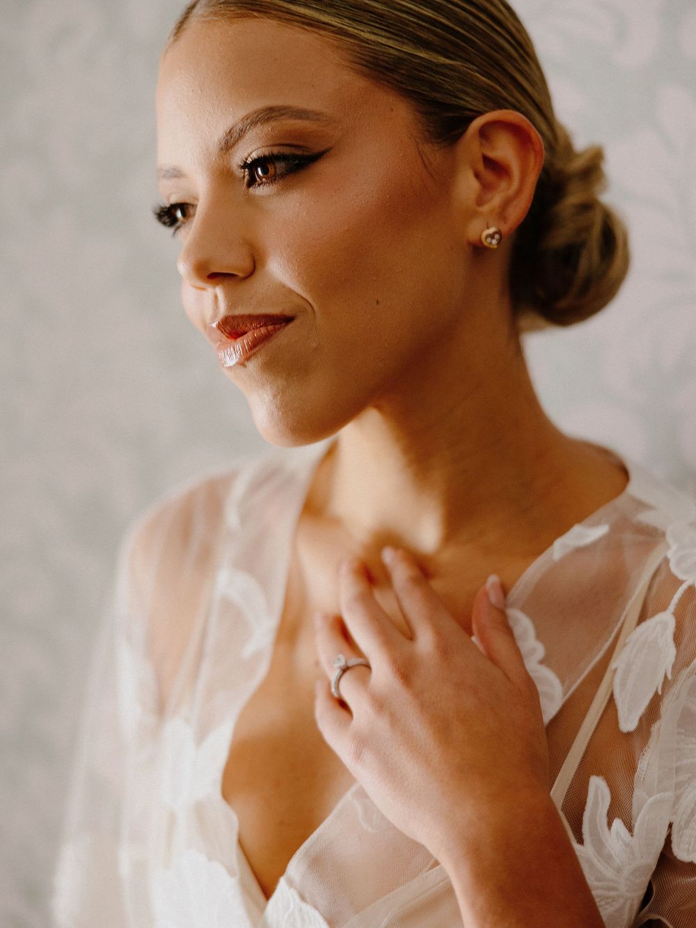 Close-up of bridal makeup featuring elegant red lipstick, sleek updo, and delicate lace wedding dress detail.