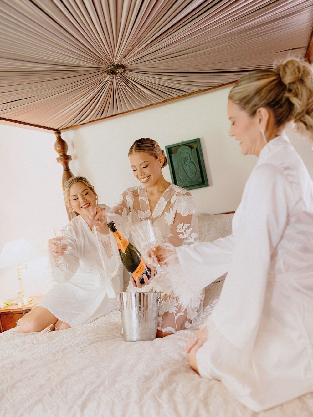 Wedding party in white robes celebrating with champagne during pre-ceremony preparations.