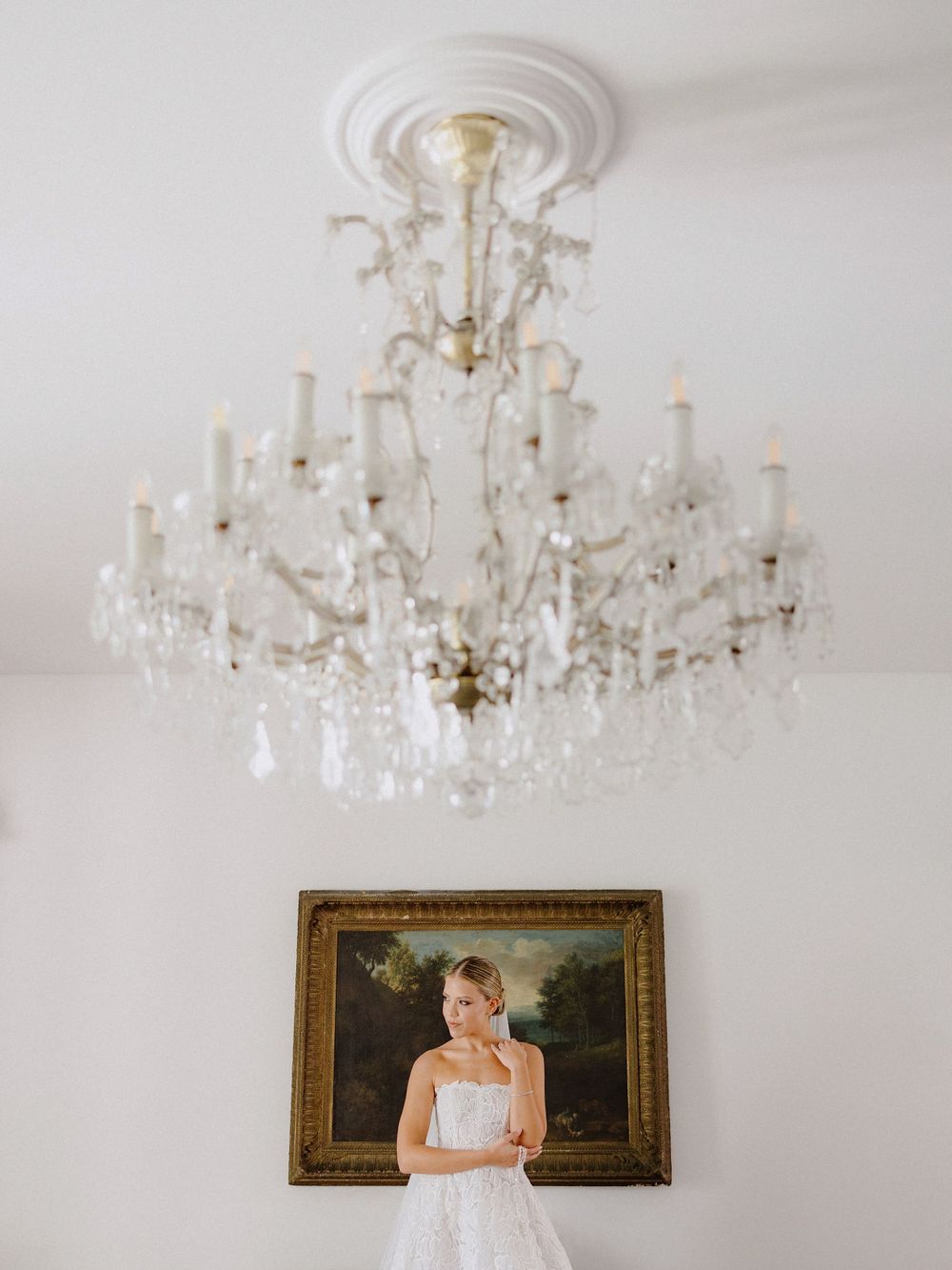 Elegant crystal chandelier hanging above bridal portrait in ornate gold frame.
