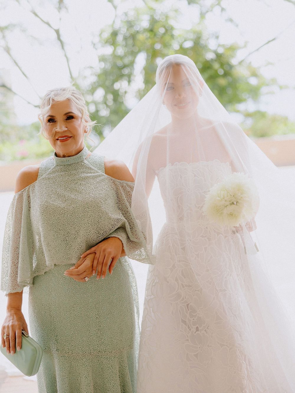 Attendant in sage green dress poses with bride in white gown and veil.
