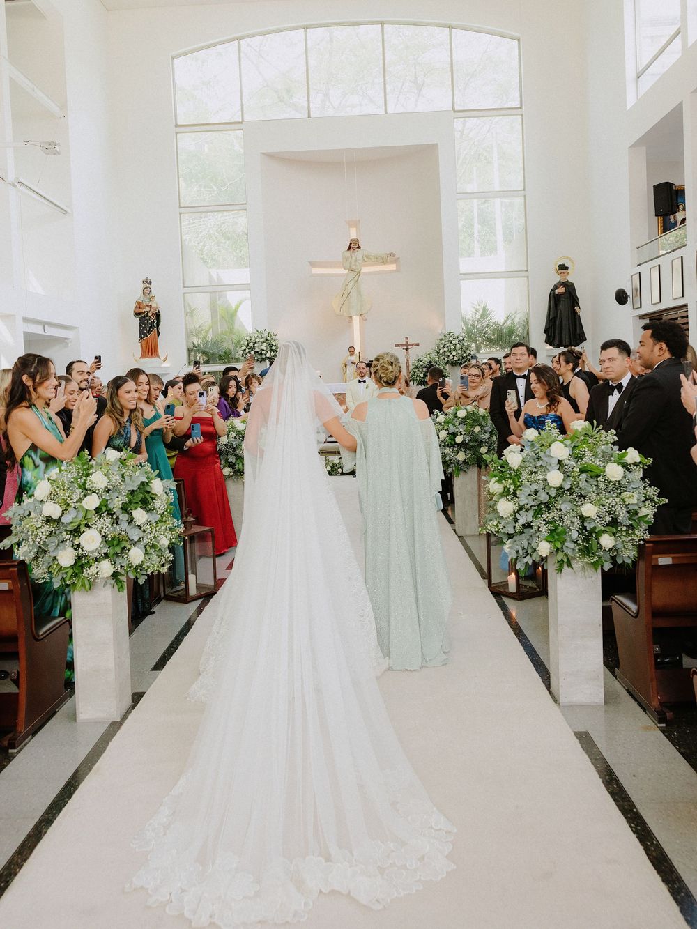 Church wedding ceremony with floral arrangements and guests watching bride walk down the aisle.