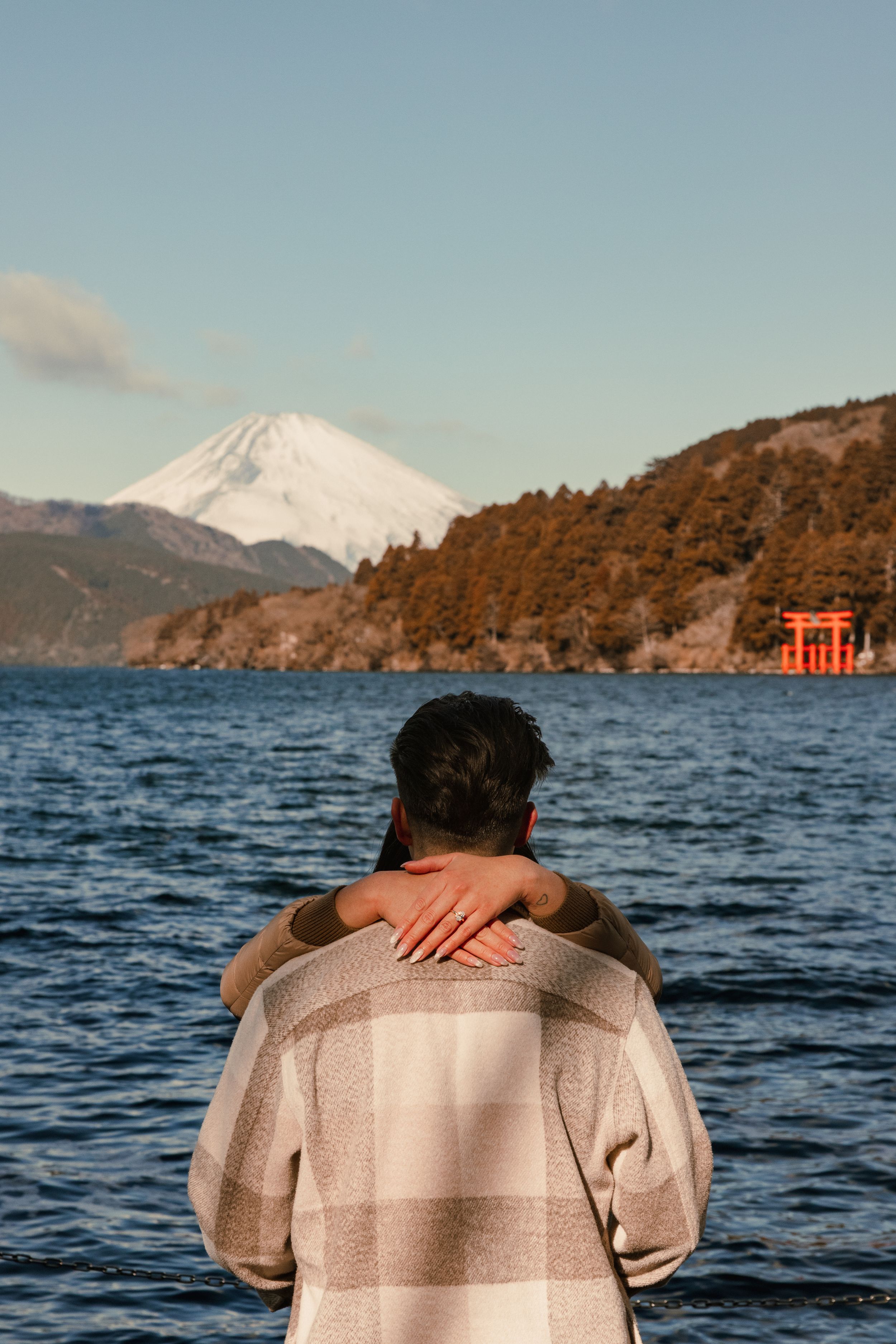Newly engaged couple enjoying view of Mount Fuji and red torii gate across Lake Ashinoko in Hakone, Japan.
