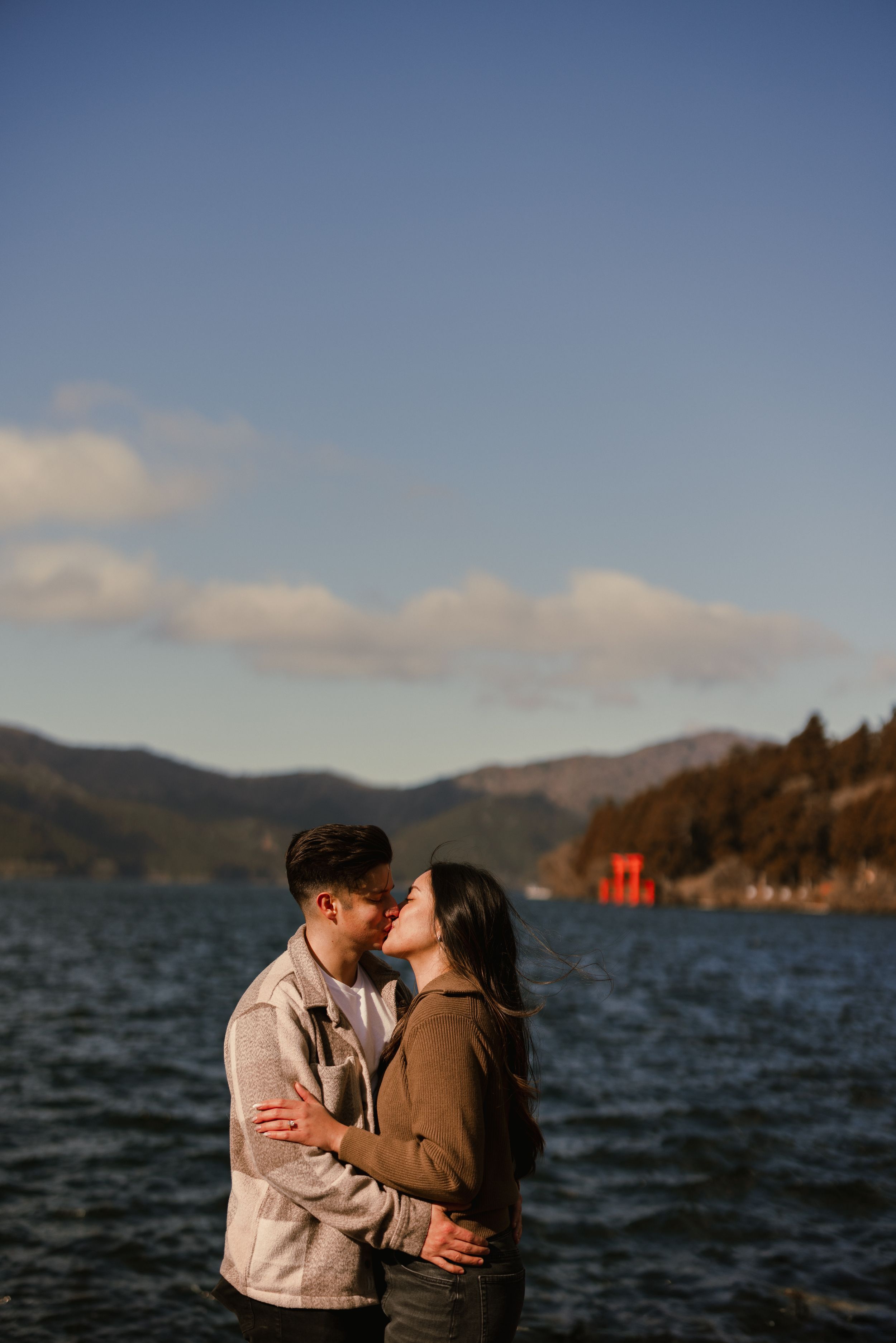 Newly engaged couple enjoying view of Mount Fuji and red torii gate across Lake Ashinoko in Hakone, Japan.