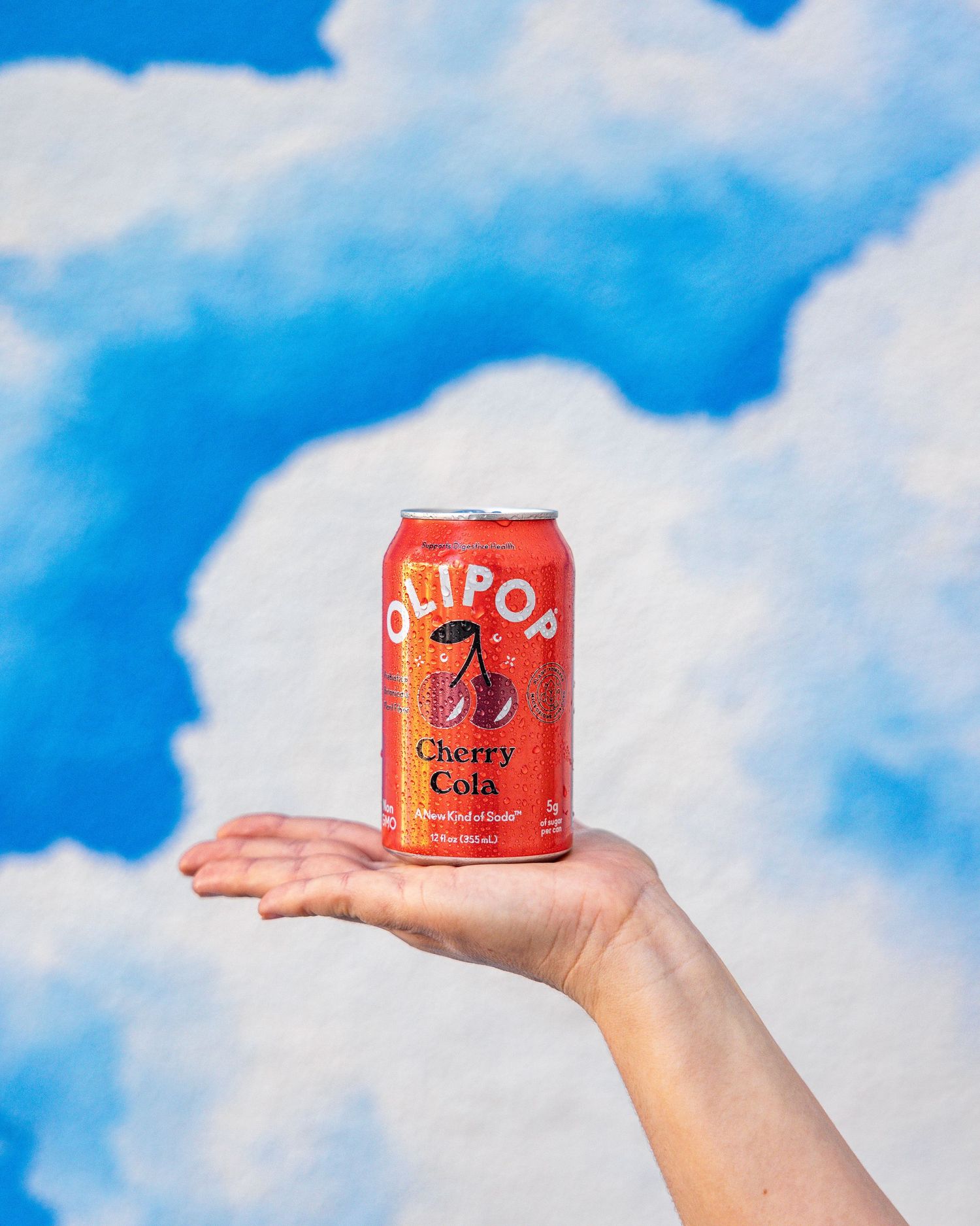 Red Jetpop cherry cola can held against blue sky with white fluffy clouds.