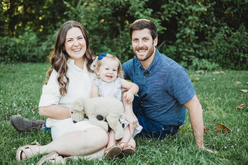 Family sitting on grass outdoors with their young child in casual summer attire.