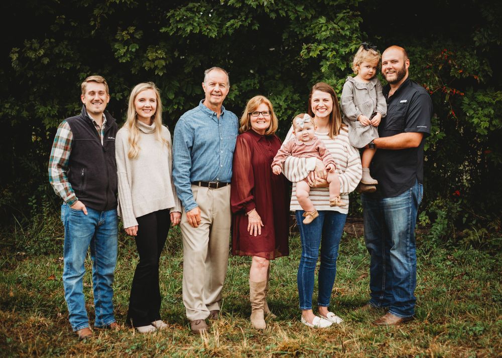 Extended family group portrait outdoors with multiple generations against autumn foliage.