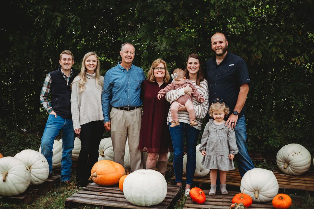 Family portrait on wooden platform decorated with white and orange pumpkins for fall.
