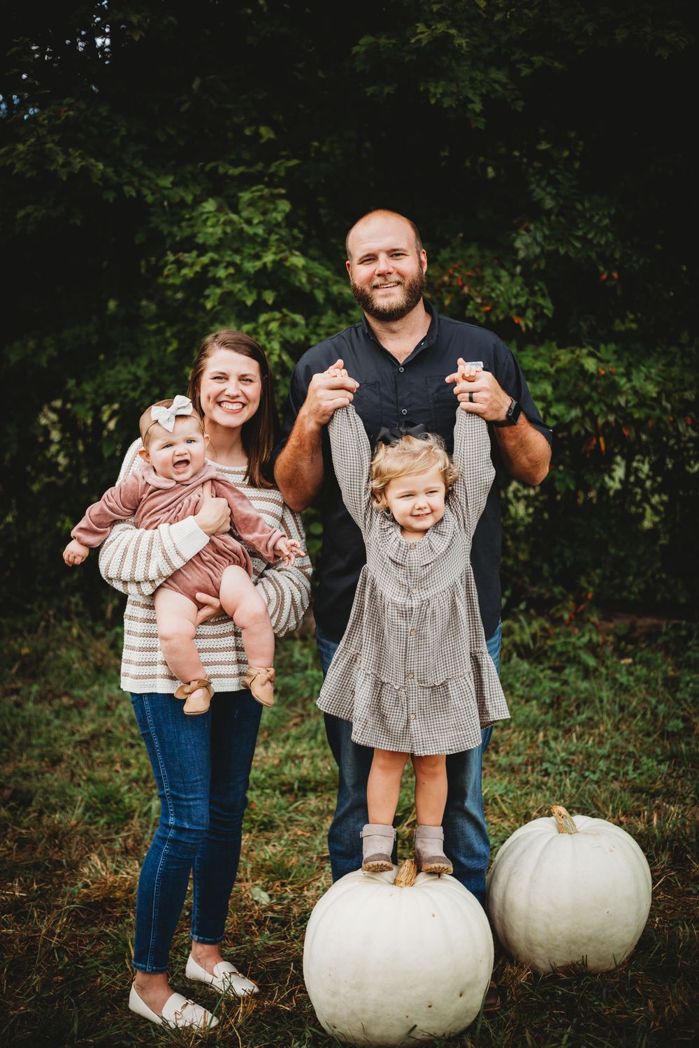 Family poses playfully on large white pumpkins during an autumn outdoor photoshoot.