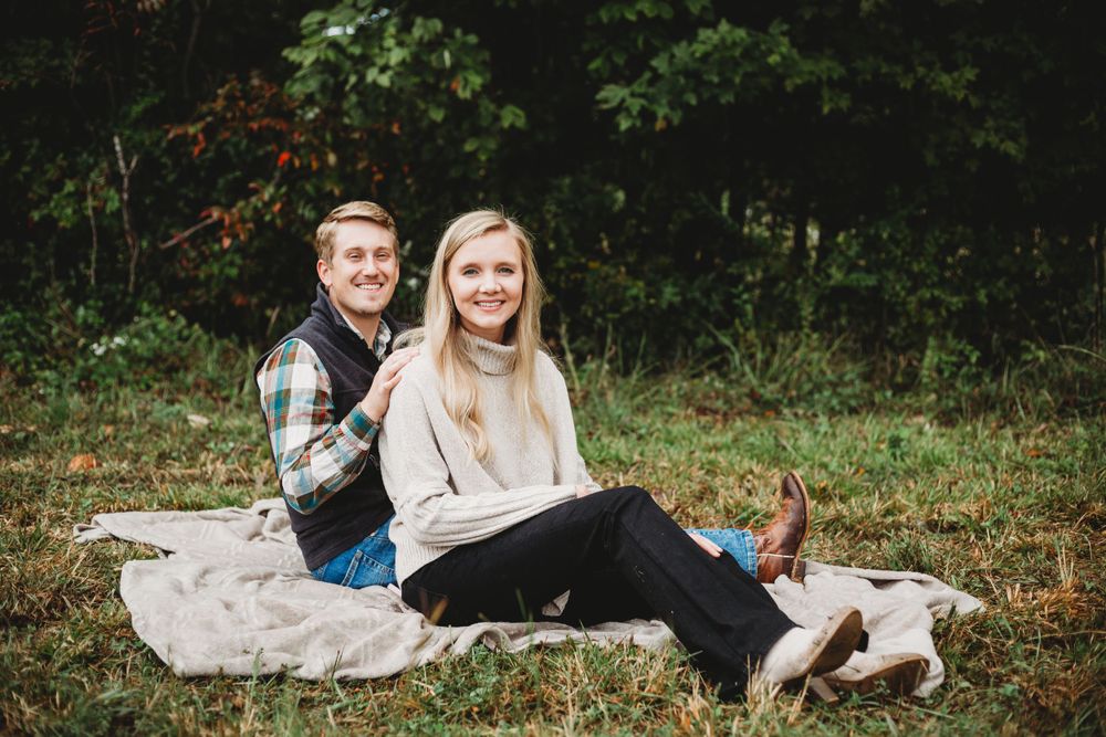 Couple relaxes on blanket during outdoor portrait session in natural setting.
