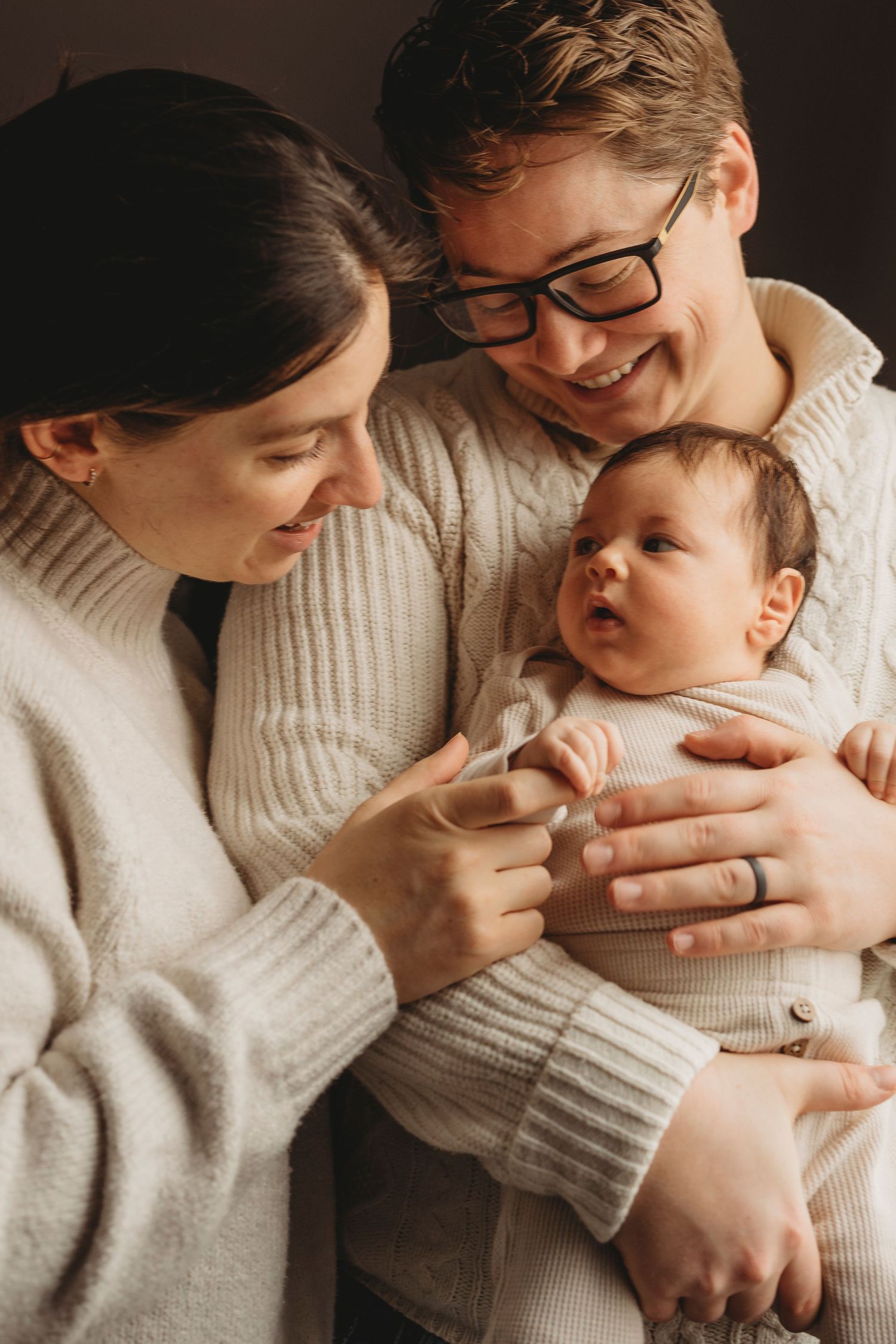 A cozy indoor family portrait featuring a newborn in warm knit sweaters.