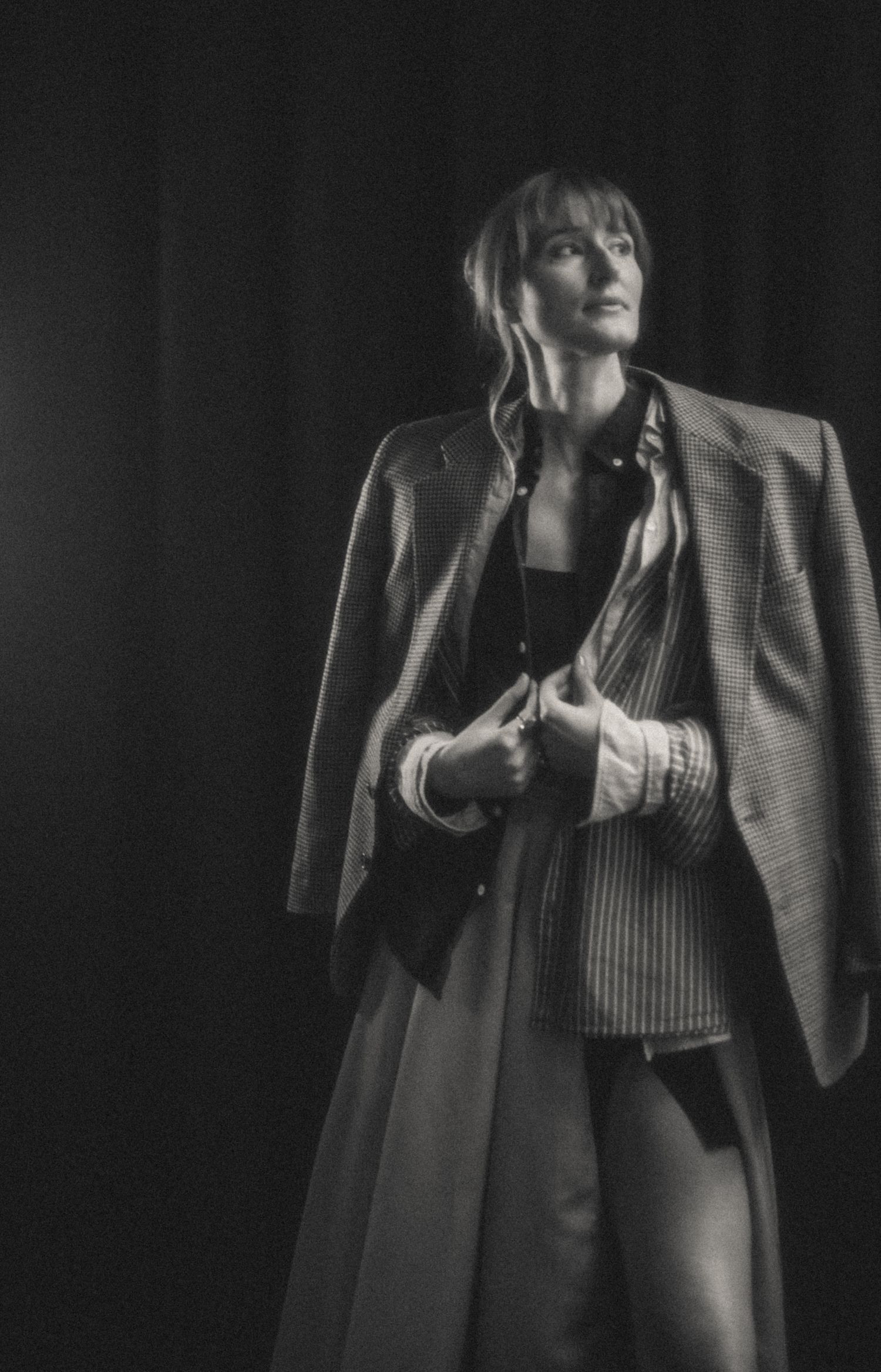 Ruta standing in a theatrical studio, wearing layered clothing with a vintage, analog-style blur.