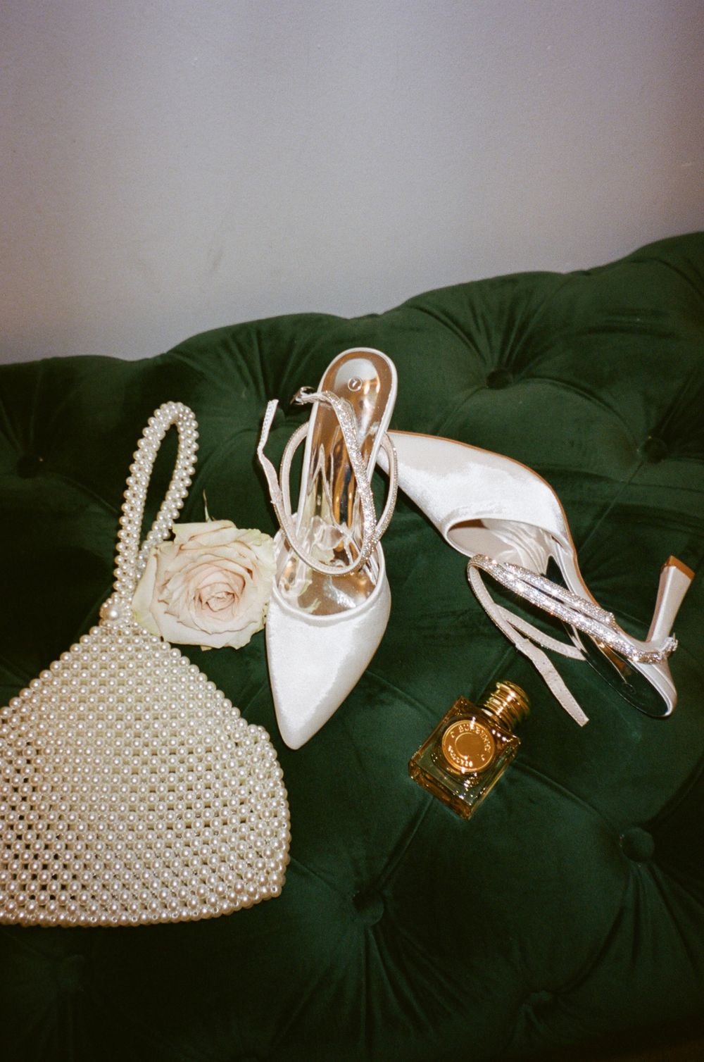 Bridal accessories arranged on dark green velvet surface including white shoes and beaded purse.