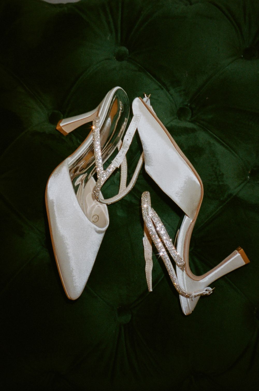 Elegant white bridal shoes with straps displayed on emerald green tufted fabric.