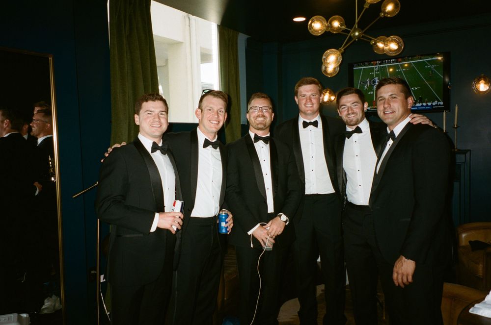 Group of men in formal black tuxedos standing together at an evening event.