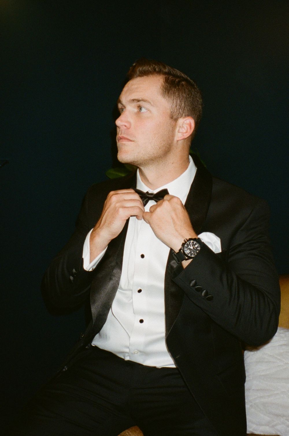 Person adjusting bowtie while wearing formal black tuxedo and watch.