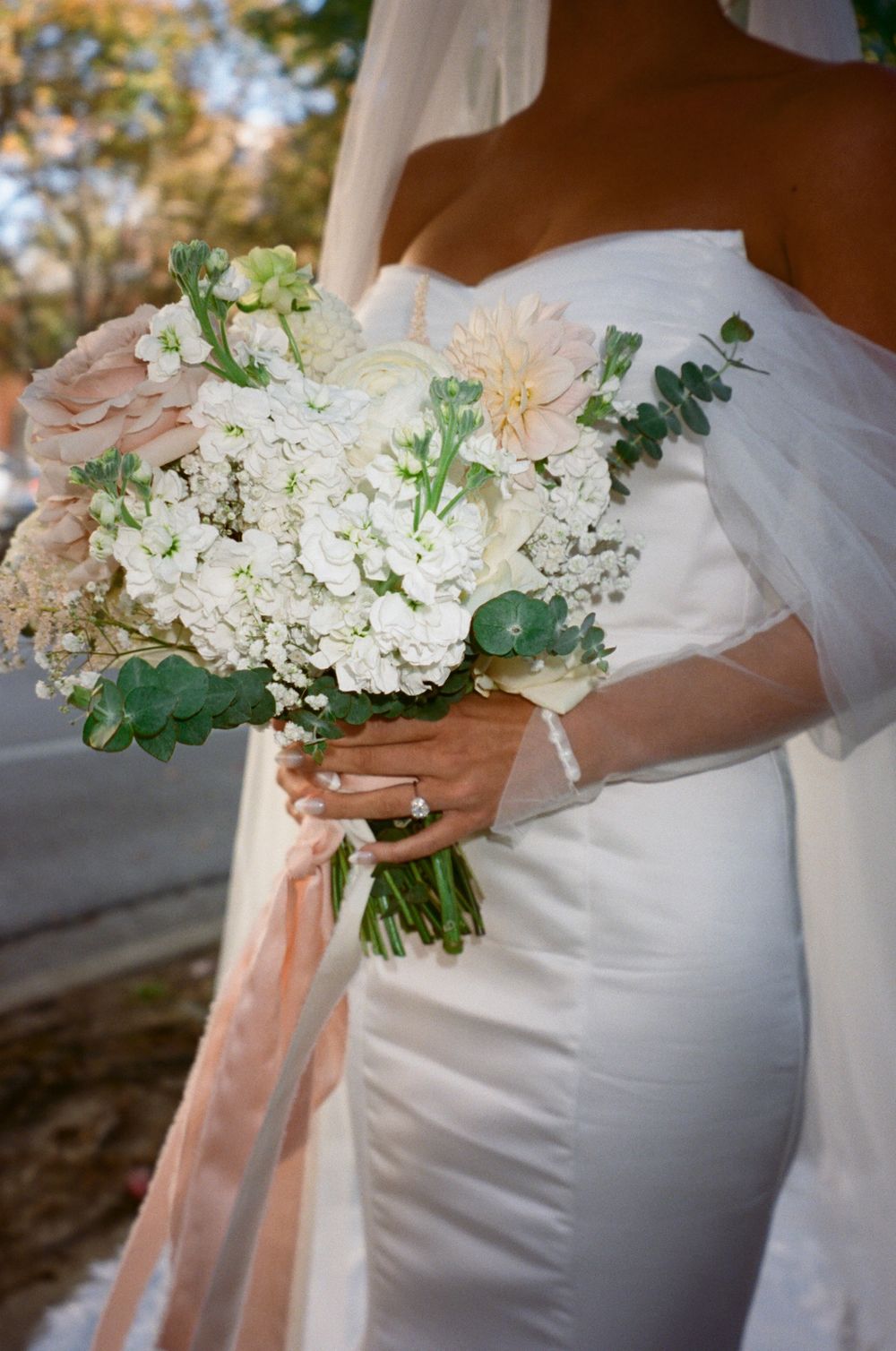 A close-up of a bridal bouquet featuring white hydrangeas and blush accents against a wedding dress.