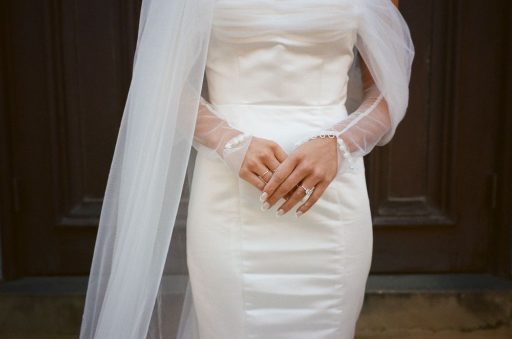 Close-up detail of a fitted white wedding dress with long sleeves and flowing veil.
