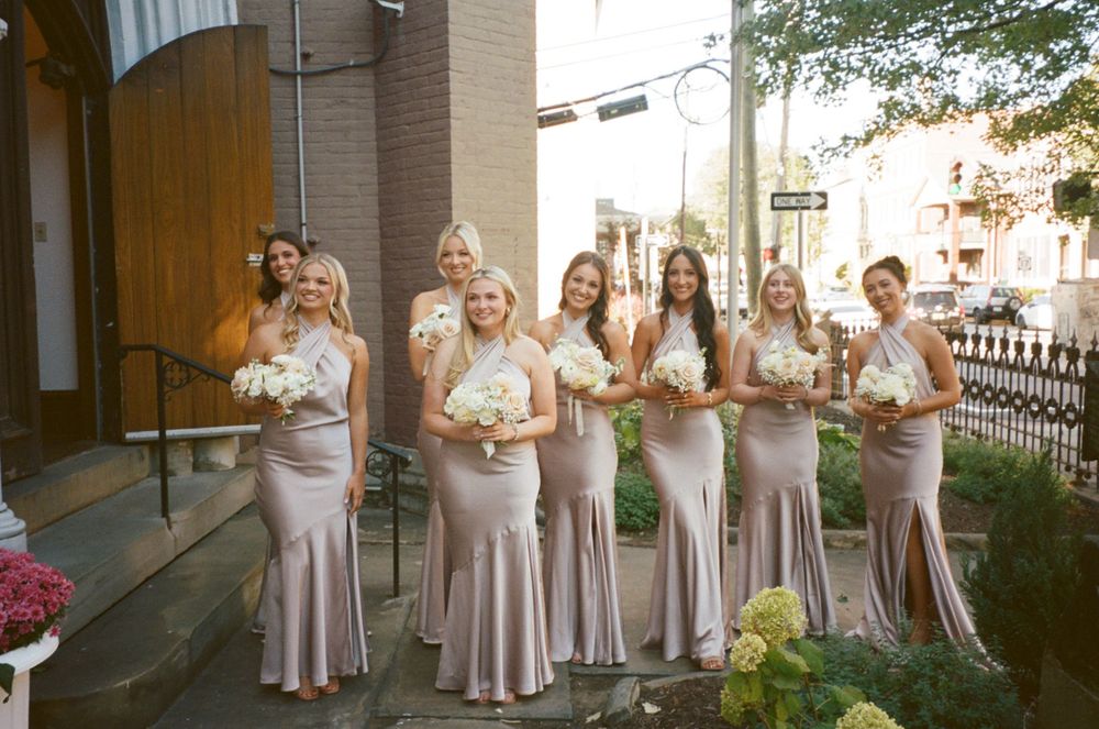 A wedding party in blush silk dresses standing together outside a church.