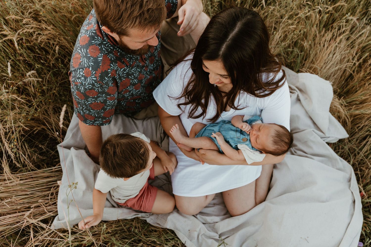 A family sits together on a blanket for a portrait session in an autumn field setting.
