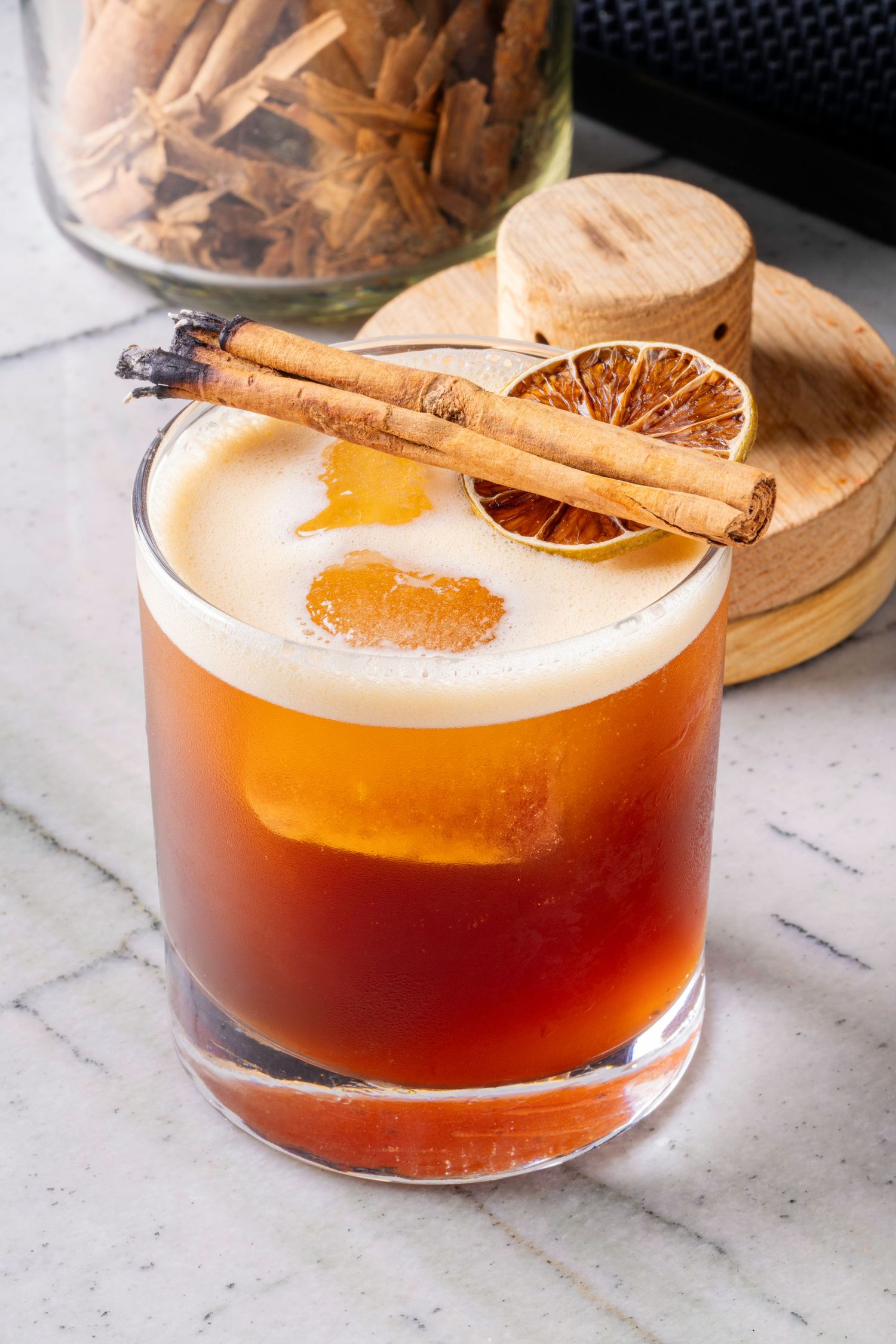 Craft cocktail garnished with cinnamon stick and dried orange slice.