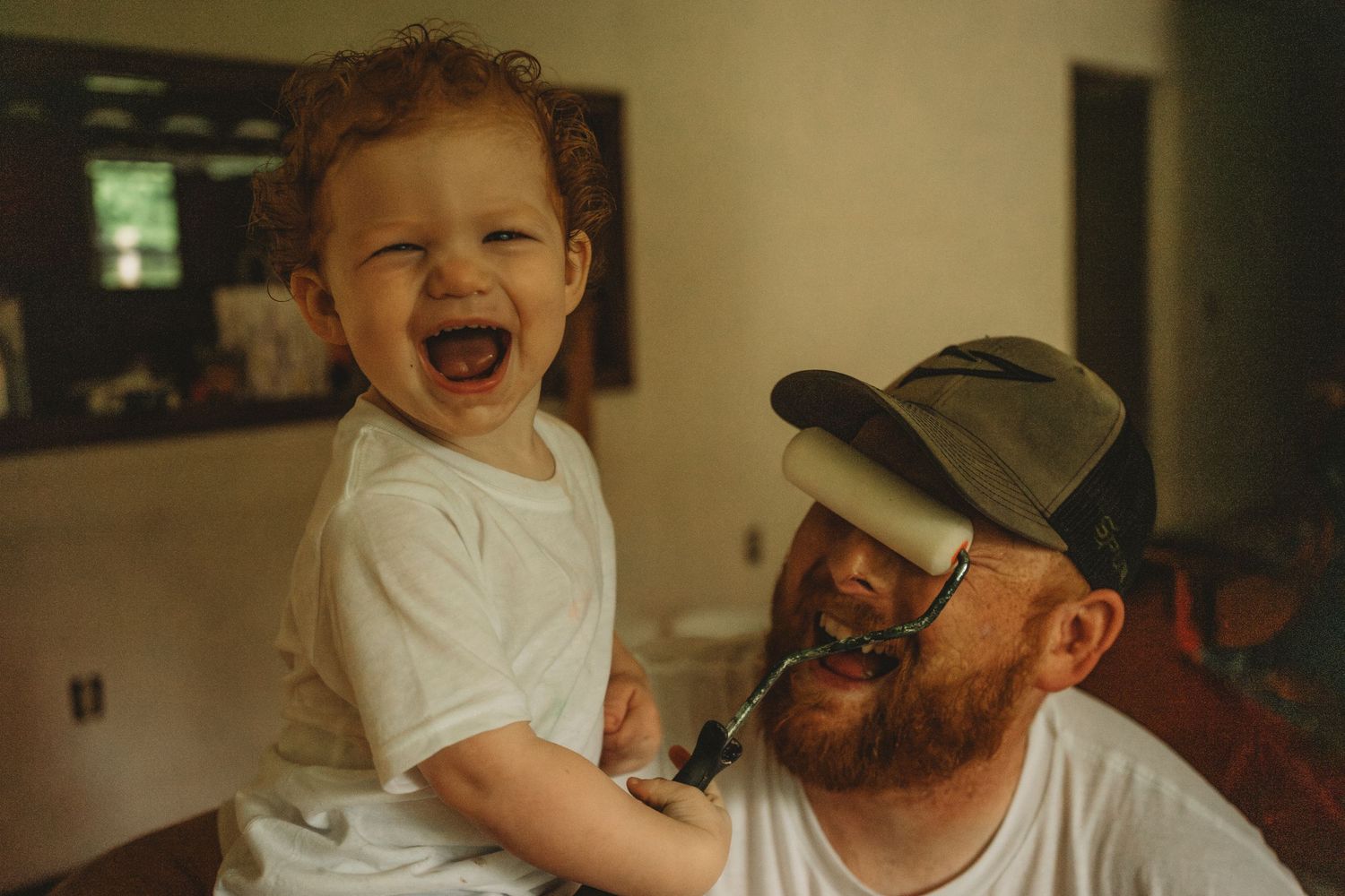A joyful moment shared between a toddler and adult wearing a baseball cap indoors.