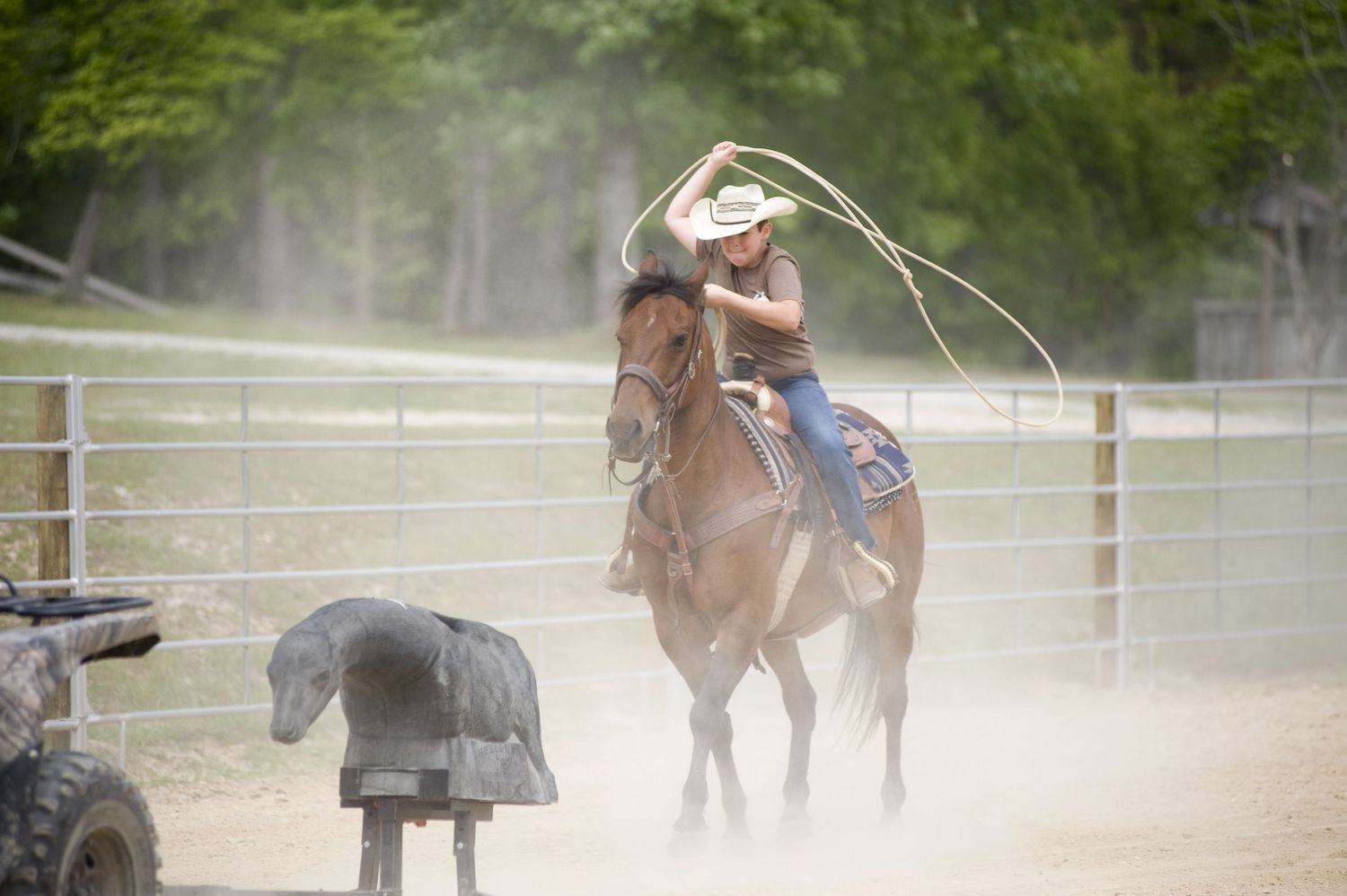 A rider practices roping skills on horseback in a dusty arena.