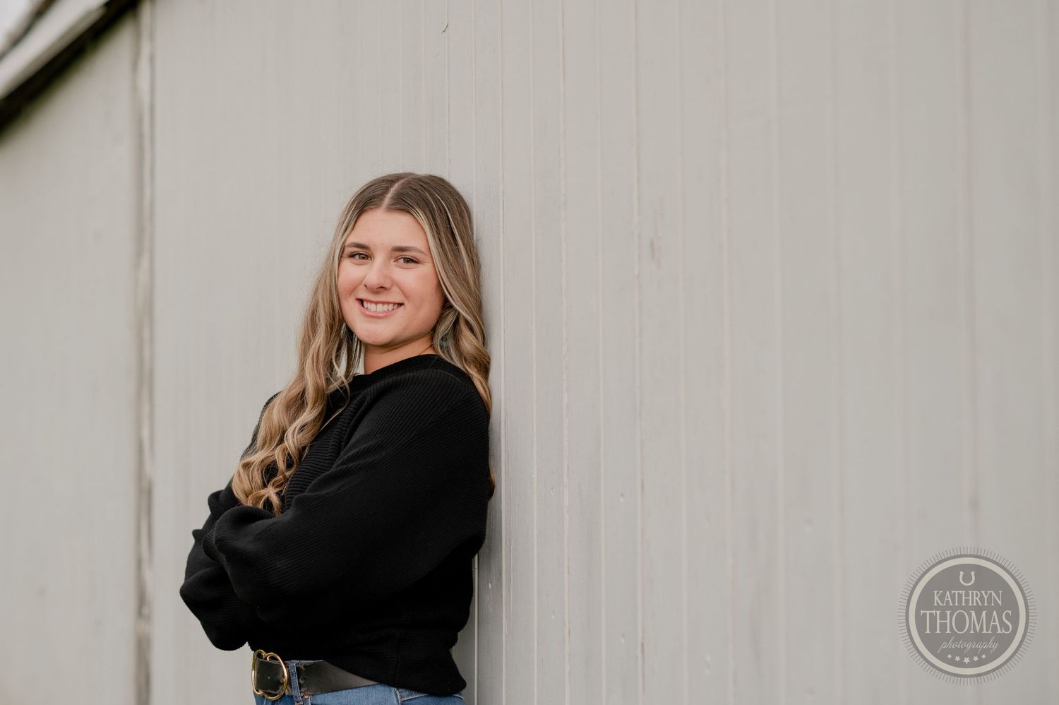 Candid outdoor shot against white wall wearing casual black sweater.