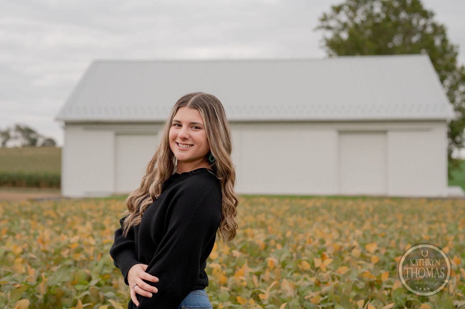 A fall photoshoot in a pumpkin field with a white barn in the background on an overcast day.