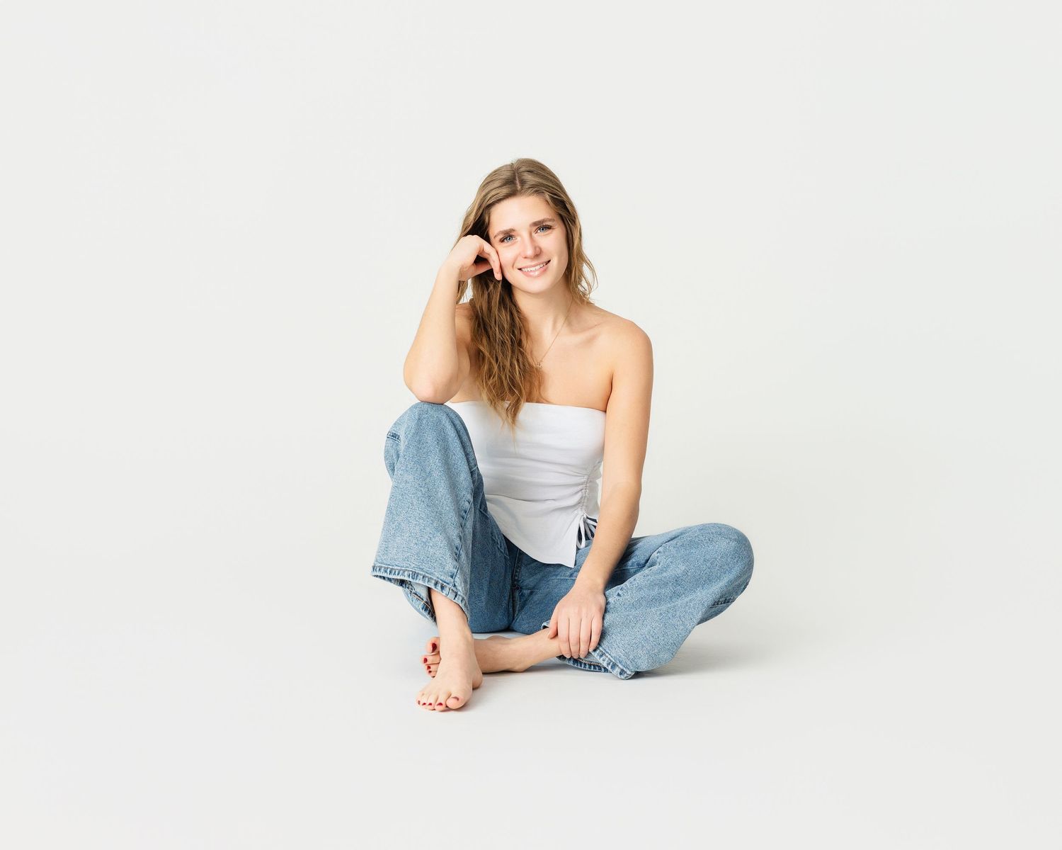 Woman in cozy white cardigan and jeans poses against autumn forest backdrop with warm lighting.