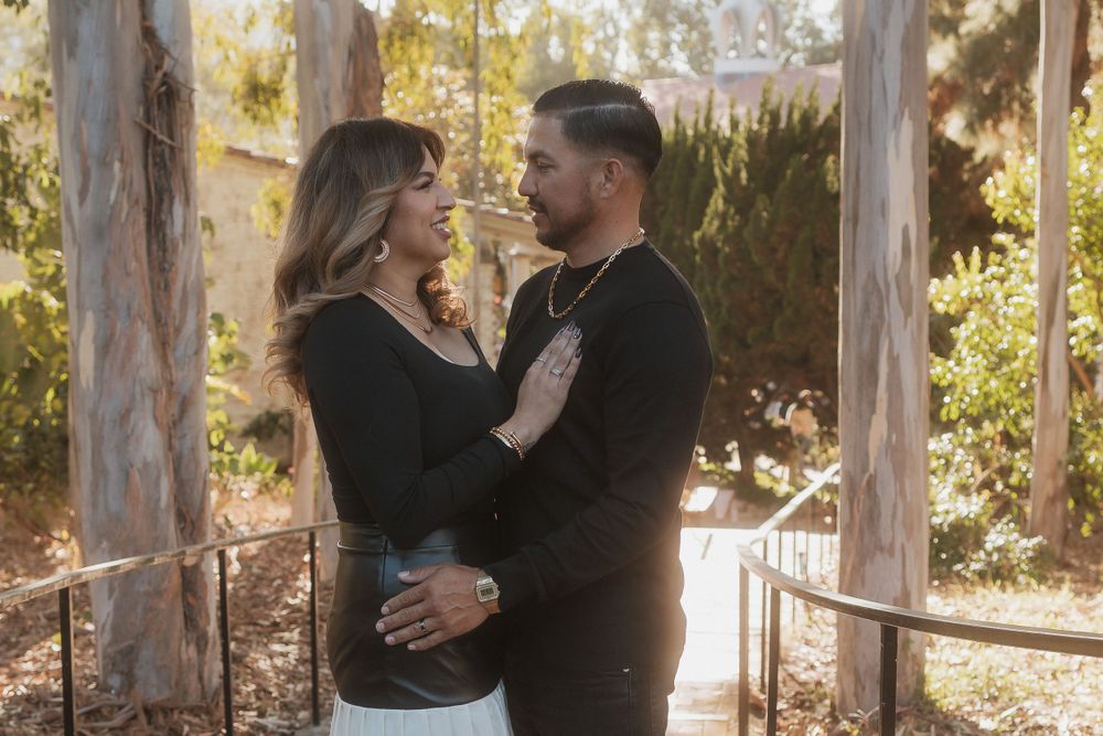 A romantic couple embraces on a brick pathway surrounded by trees and natural lighting.