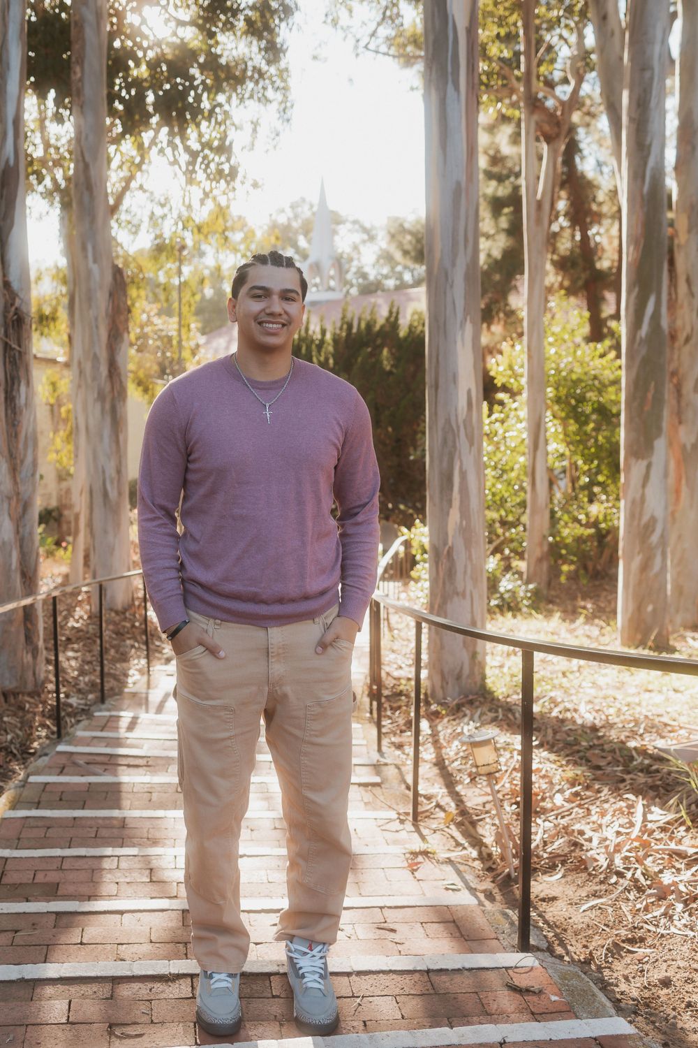A person in a lavender sweater poses casually on brick steps outdoors.