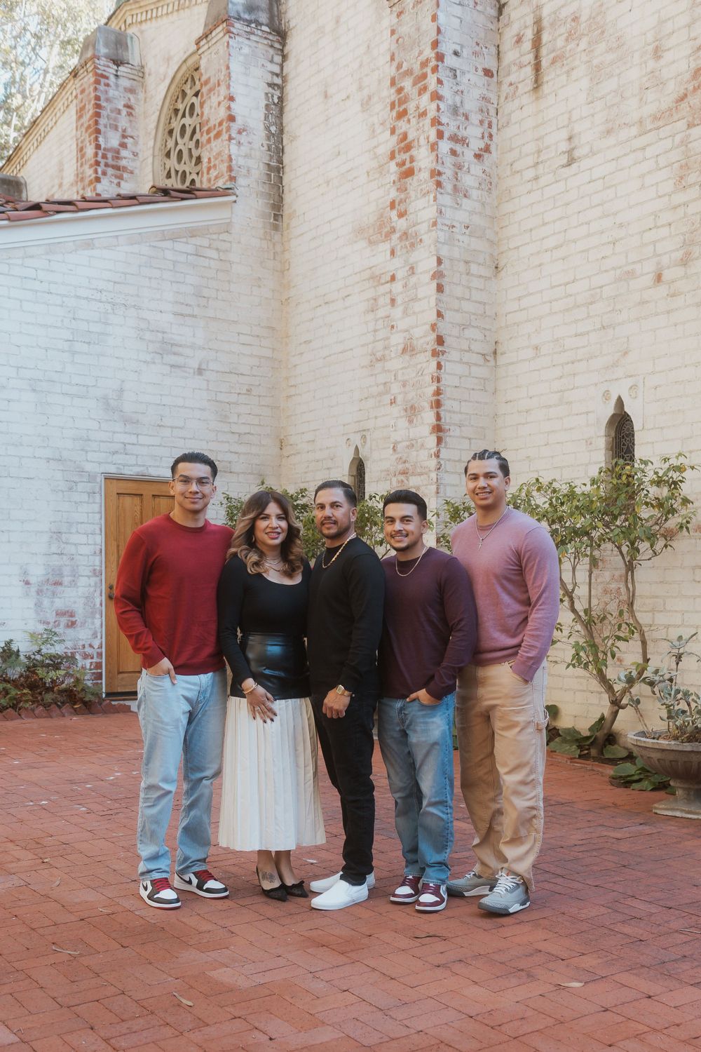 Five people pose together in front of a white brick wall with architectural details.