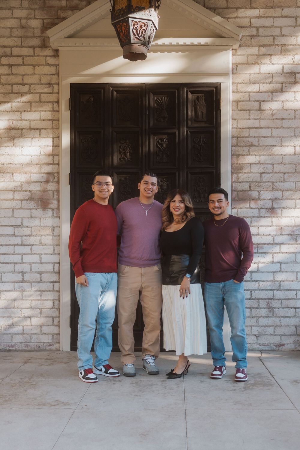 Four people pose in front of an ornate wooden door and brick entrance.
