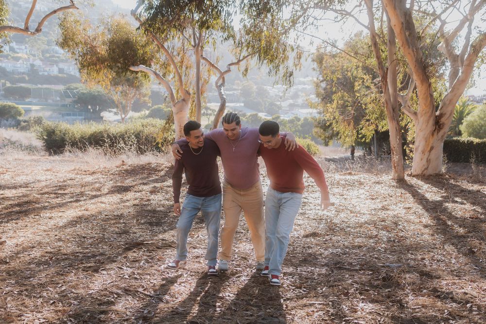 Three friends having fun posing together outdoors in a wooded area on a sunny day.
