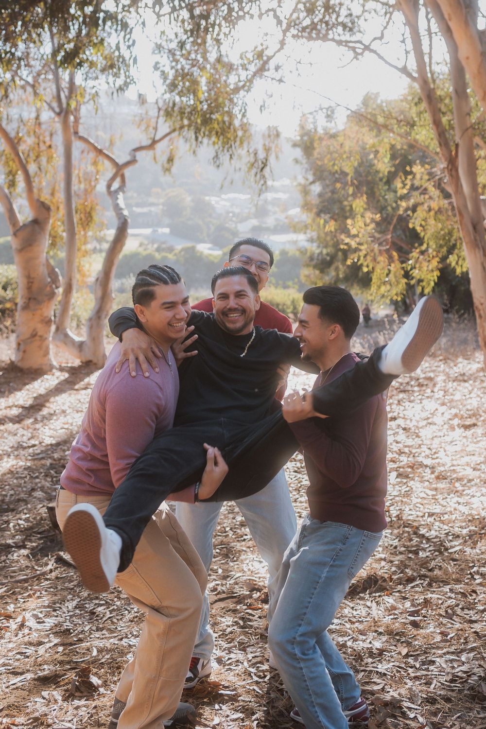 Group of friends laughing while lifting and carrying one person in a playful outdoor photoshoot.