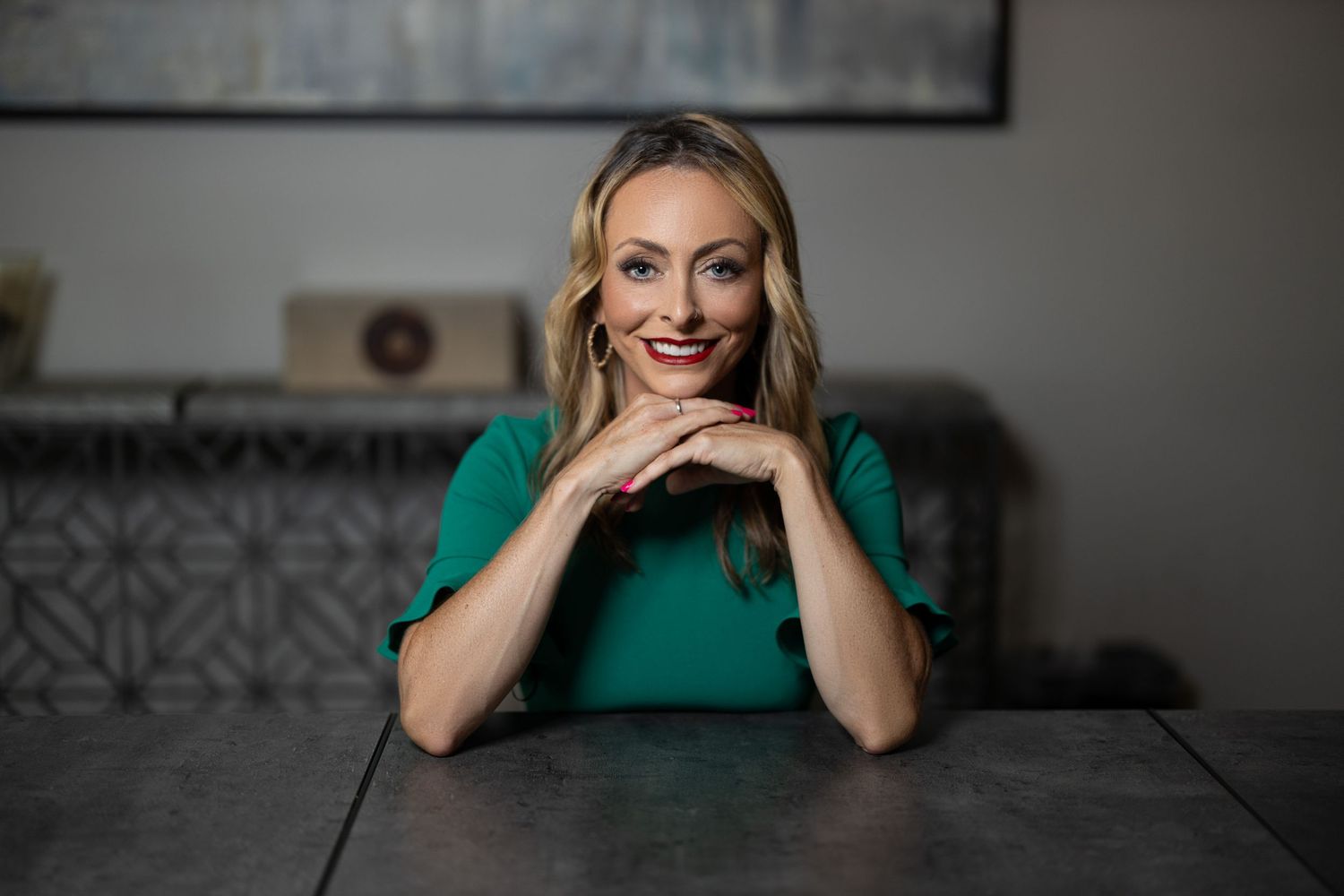 Professional headshot with someone smiling with hands under chin at table.
