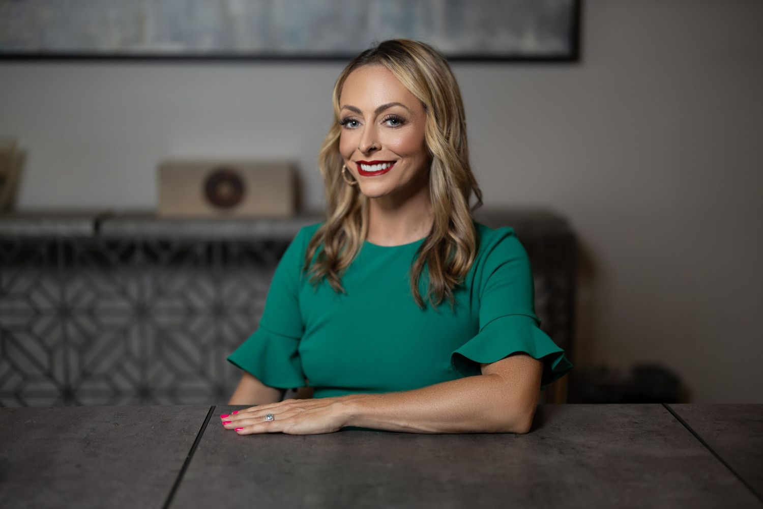 Business portrait of someone in green dress seated at dark table.