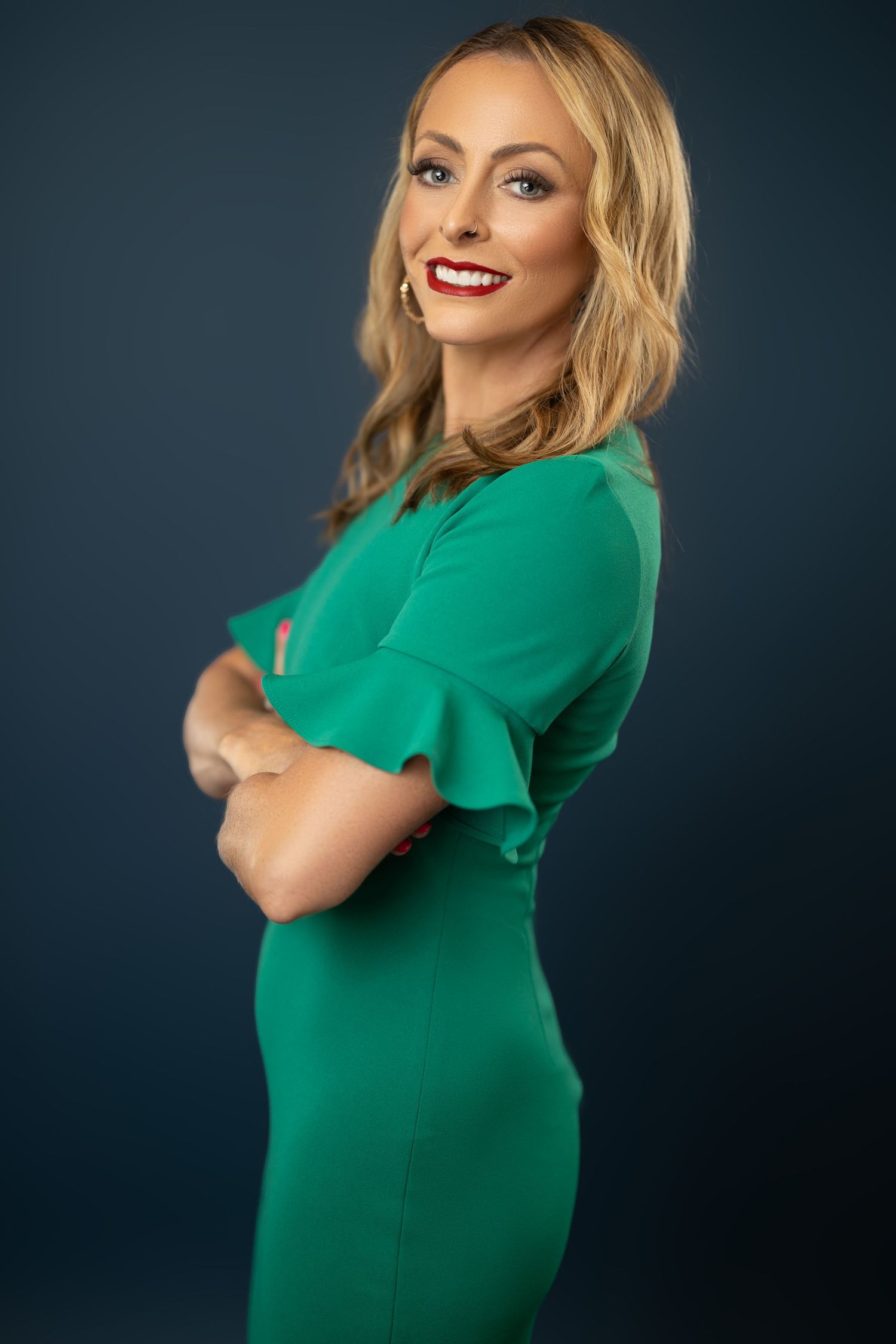 Professional portrait of a model in an emerald green dress posing against a dark background.