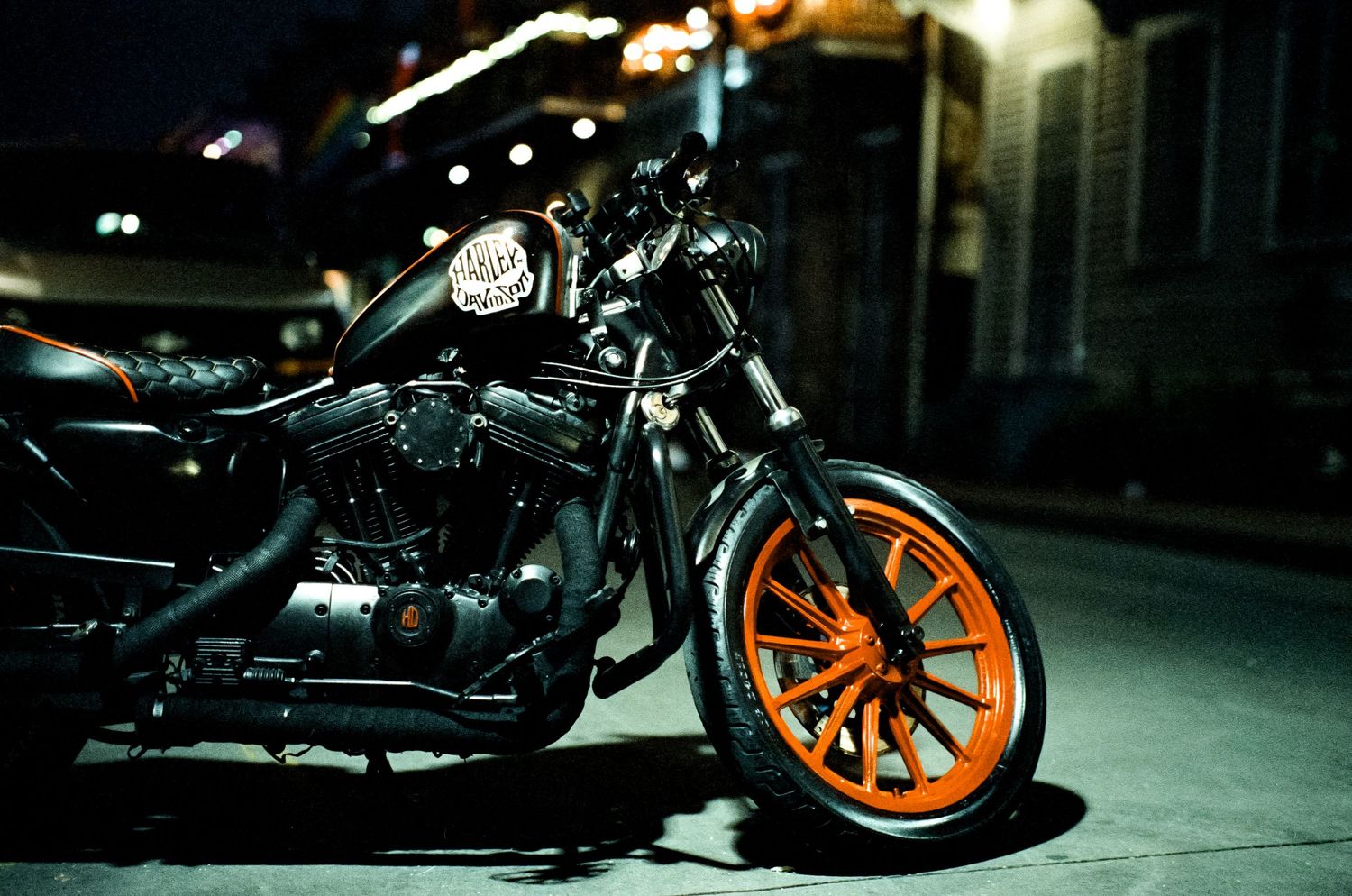 A sleek black motorcycle with orange wheels parked on a city street at night.