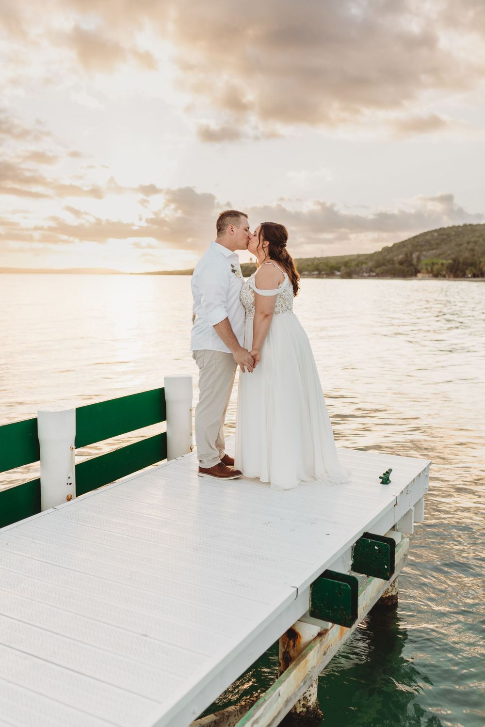 A romantic sunset photo of a couple on a white dock overlooking the ocean.