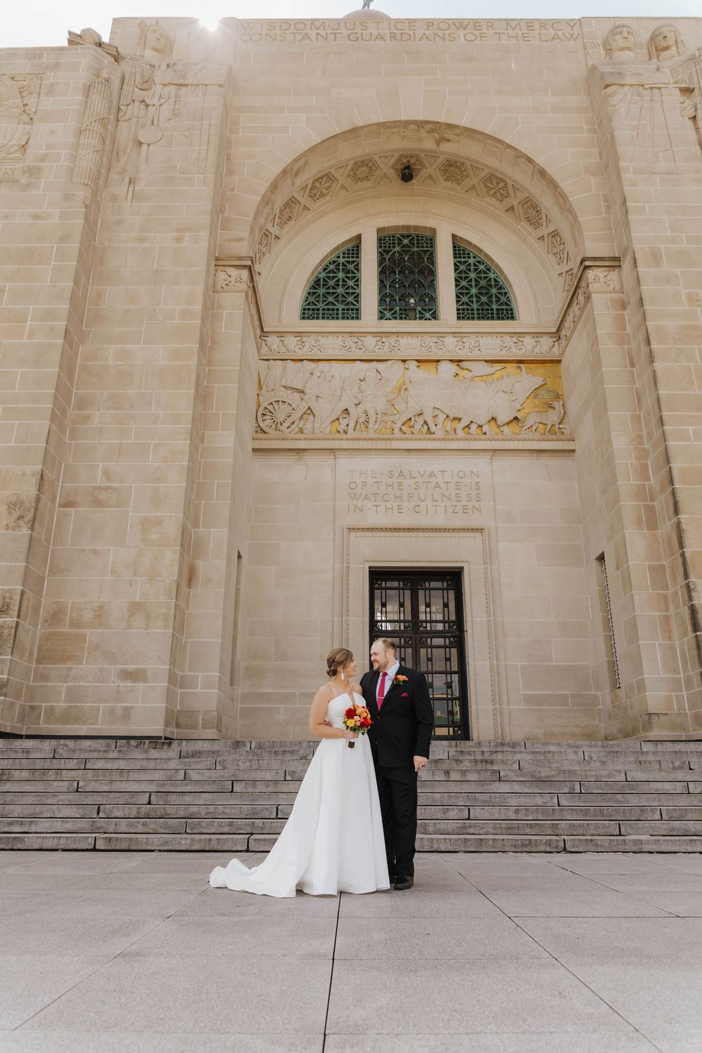 Elegant wedding couple stands in front of a grand stone church entrance with arched doorways and steps.