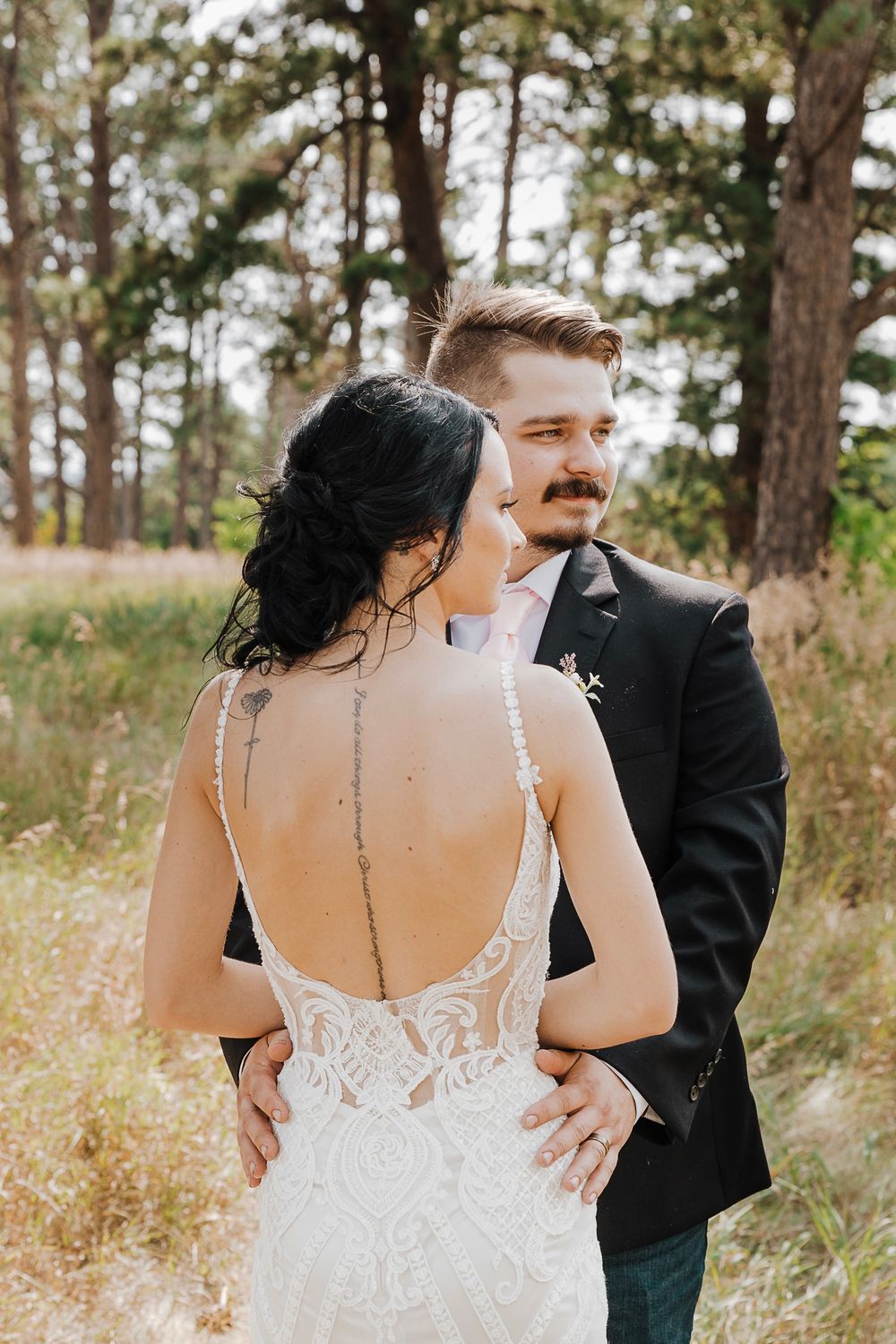 Elegant lace back wedding dress detail shown against rustic outdoor pine forest backdrop.
