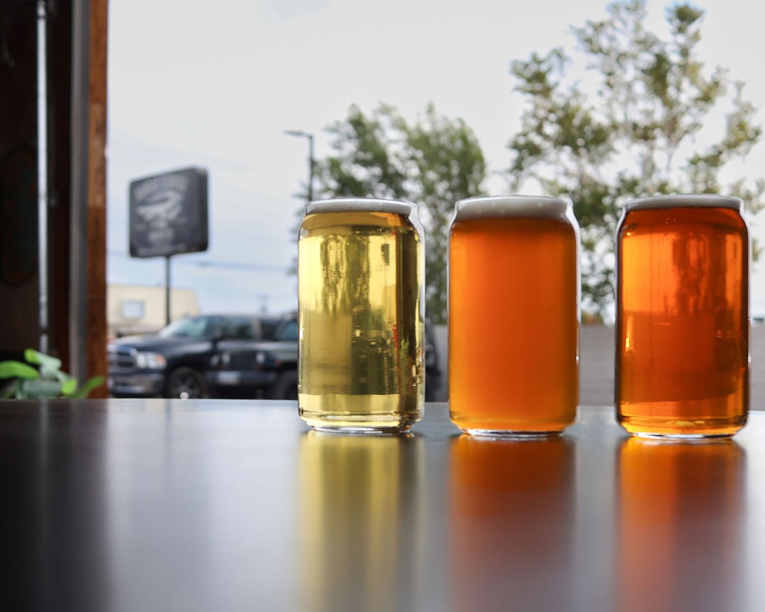 Three glasses of different colored craft beers lined up on counter with window view.