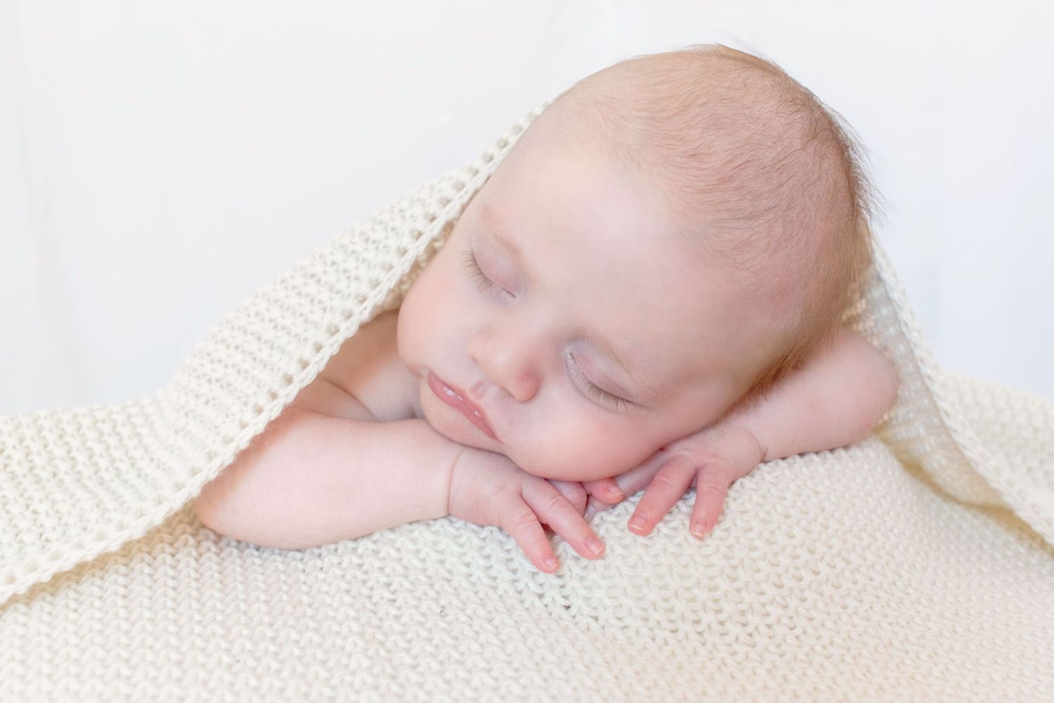Sleeping newborn wrapped in soft white blankets against light background in series of peaceful poses.
