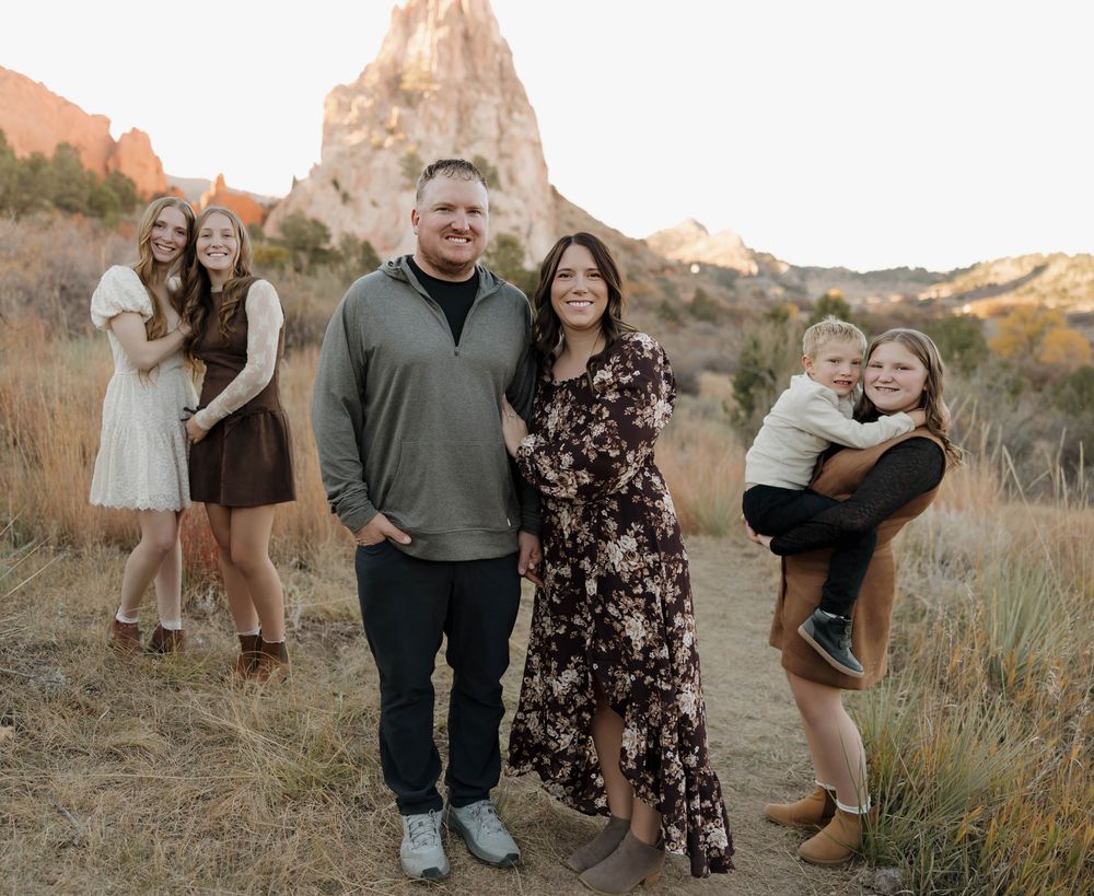 A group poses together outdoors during golden hour in a desert landscape with red rocks and brush in the background.